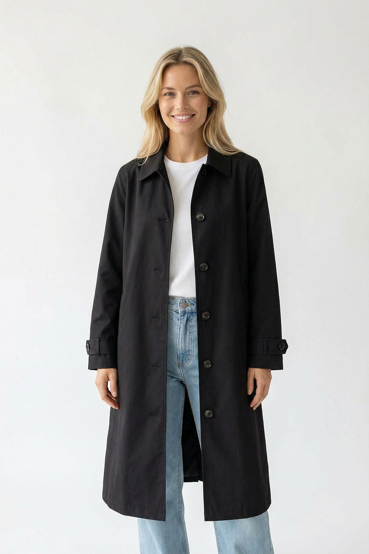 Sort oversize trenchcoat med knapper og lange ærmer over hvid t-shirt og lyseblå jeans.