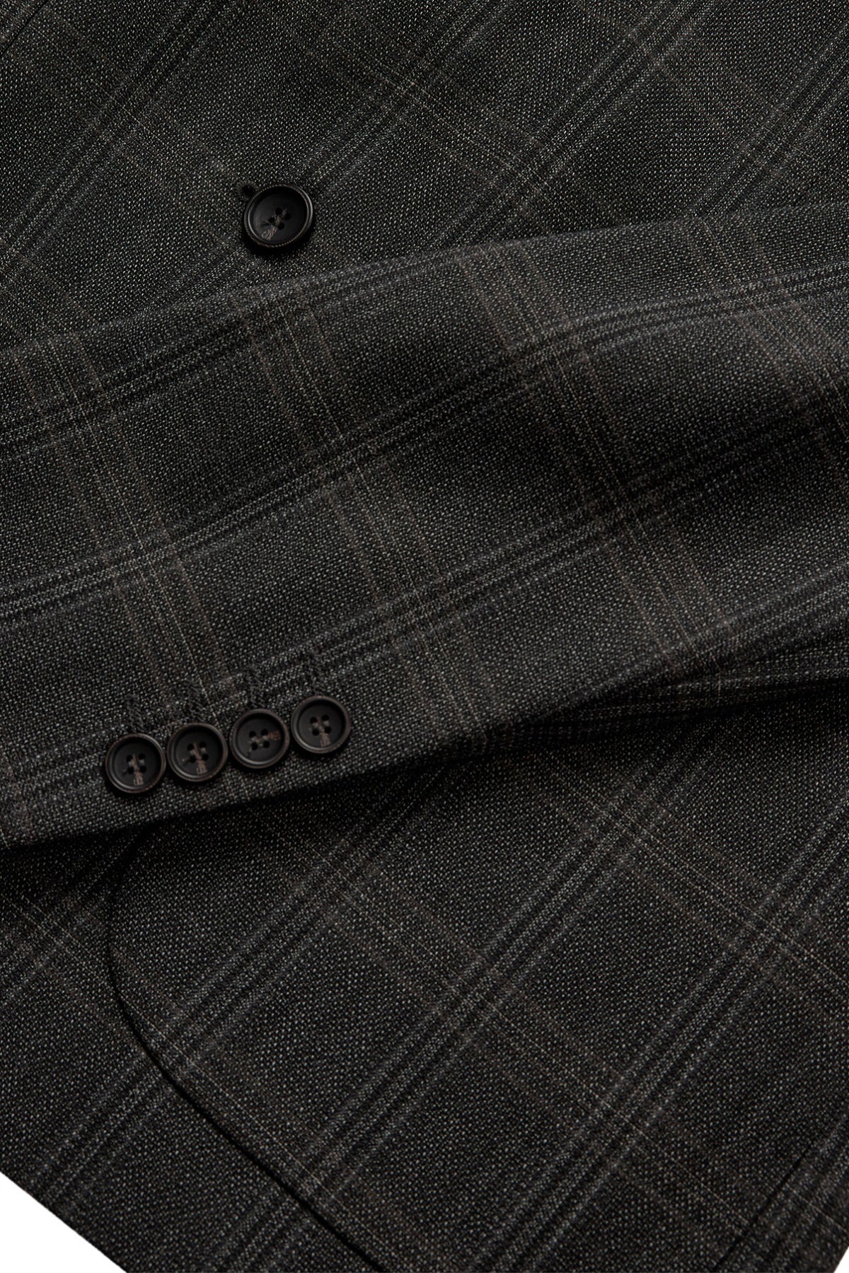 Detaljeret close-up af brun ternet uldblazer med knapper på ærmet og fint vævet mønster.