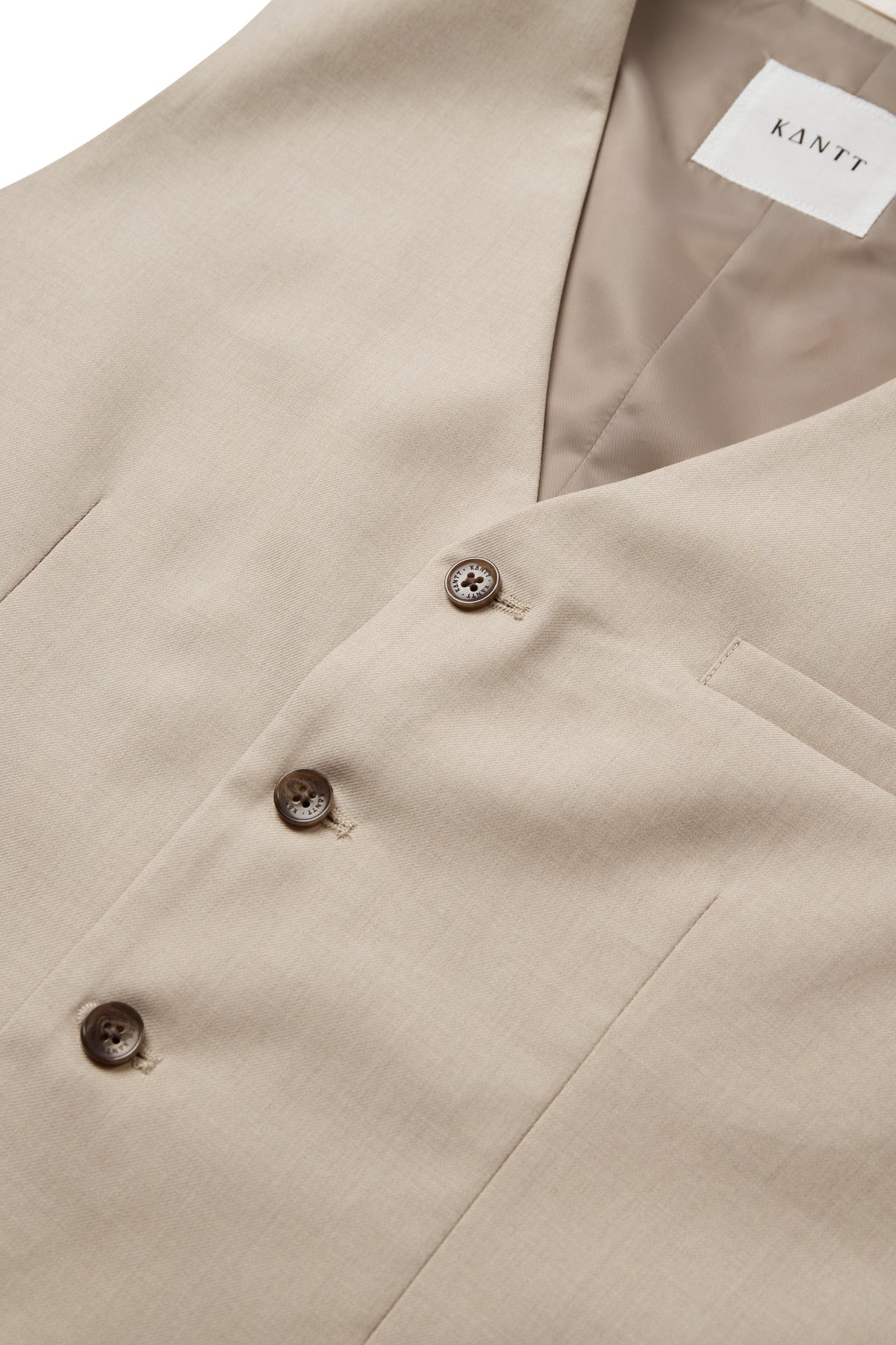 Beige vest med V-hals, paspolerede lommer og mørke knapper i to rækker.