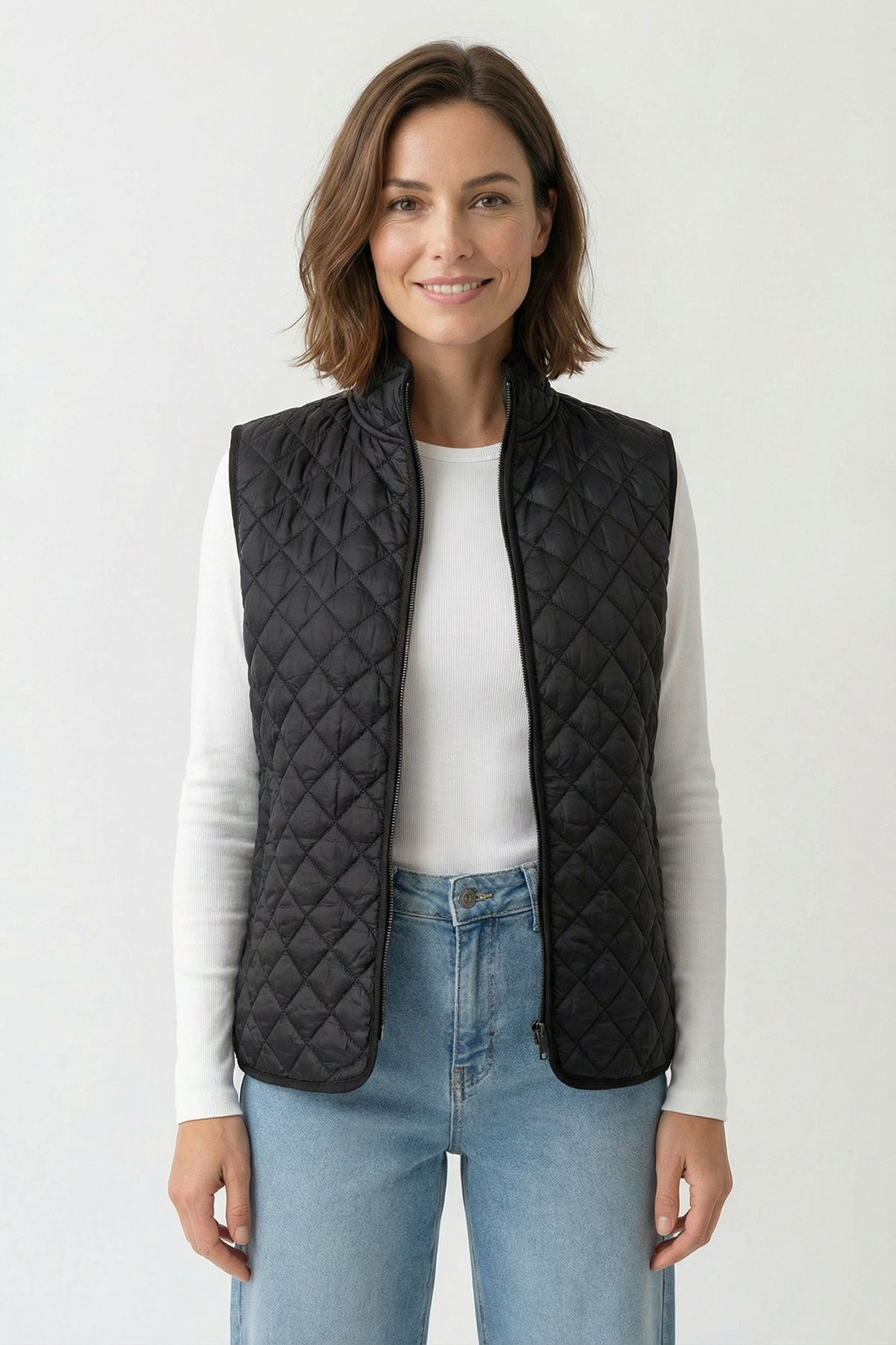 Sort let quiltet vest med lommer og rund hals, båret over hvid bluse og blå jeans.