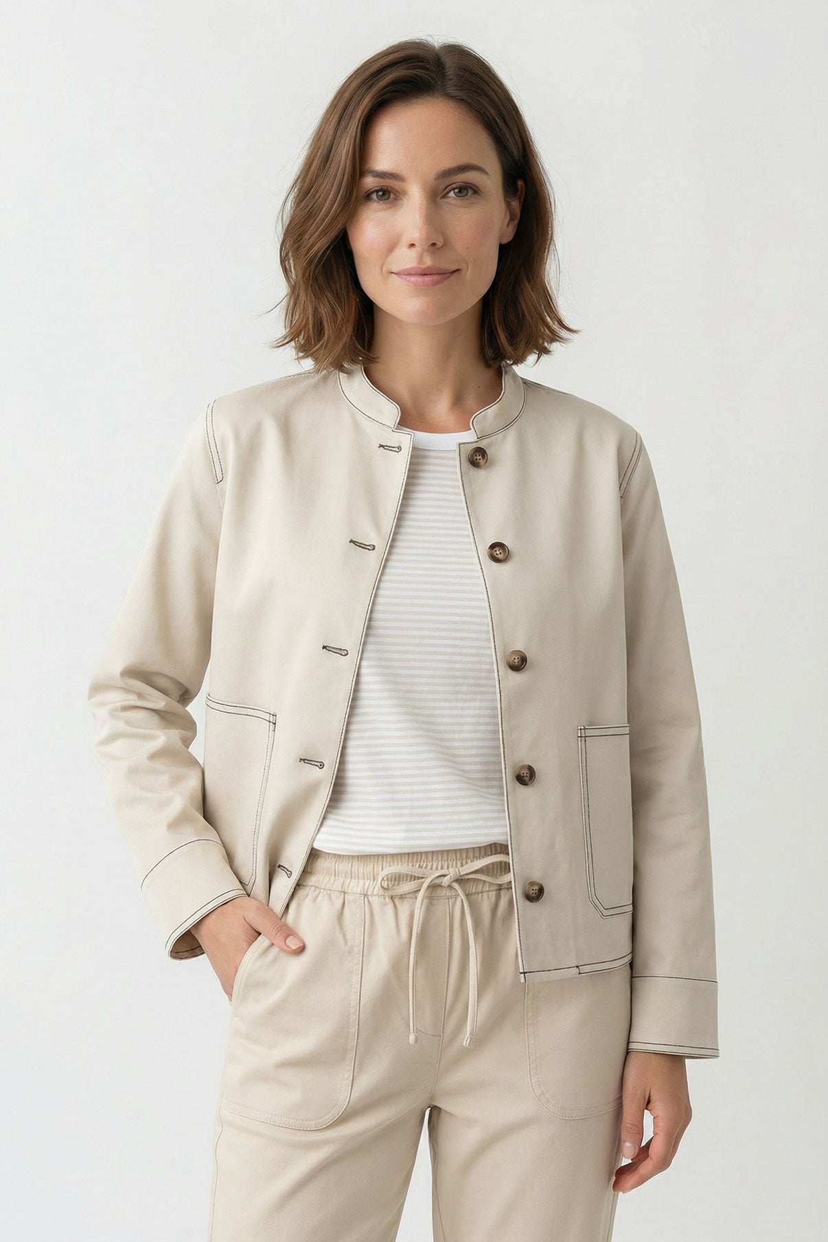 Lysegrå jakke med frontlommer og knaplukning i blødt materiale, model iført hvid top og beige bukser.