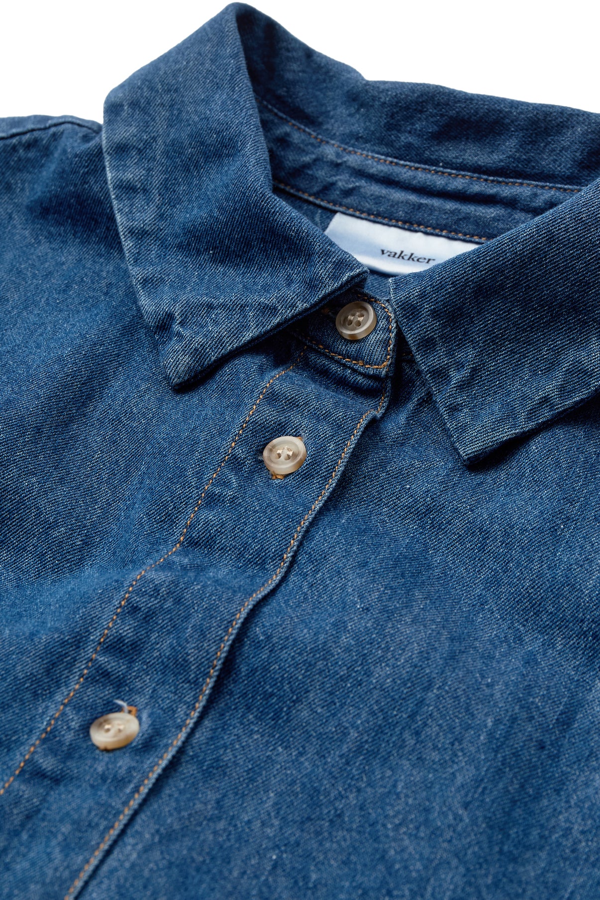 Mørkblå denimskjorte med trekvartærmer og beige knapper i tæt udsnit.