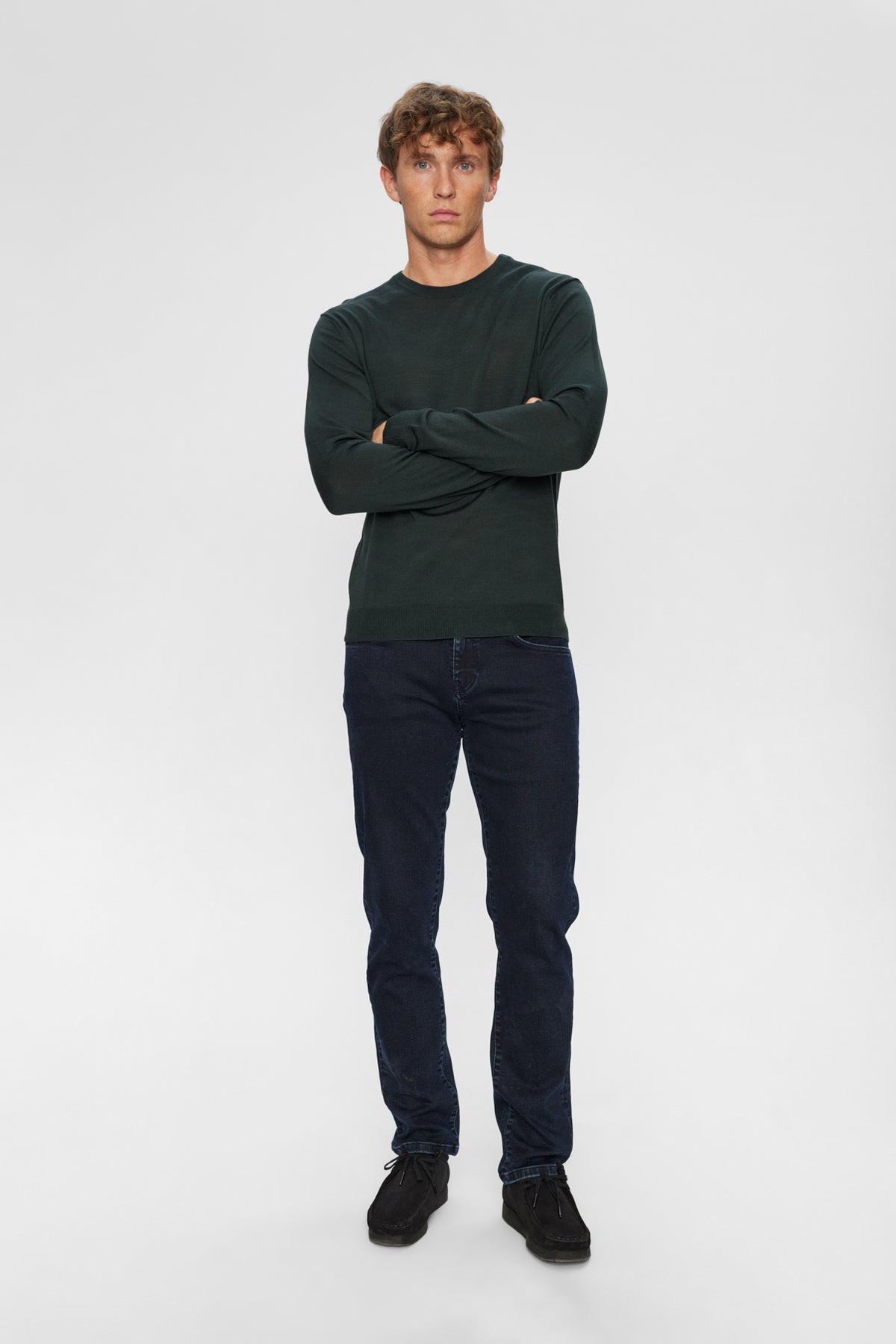 Mørkegrøn merinouldspullover med rund hals, vist med mørkeblå jeans og sorte sko.