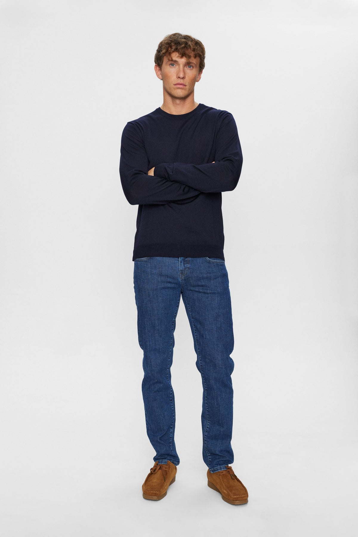 Mørkeblå merinouldspullover med rund hals, langærmet, kombineret med blå jeans og brune sko.