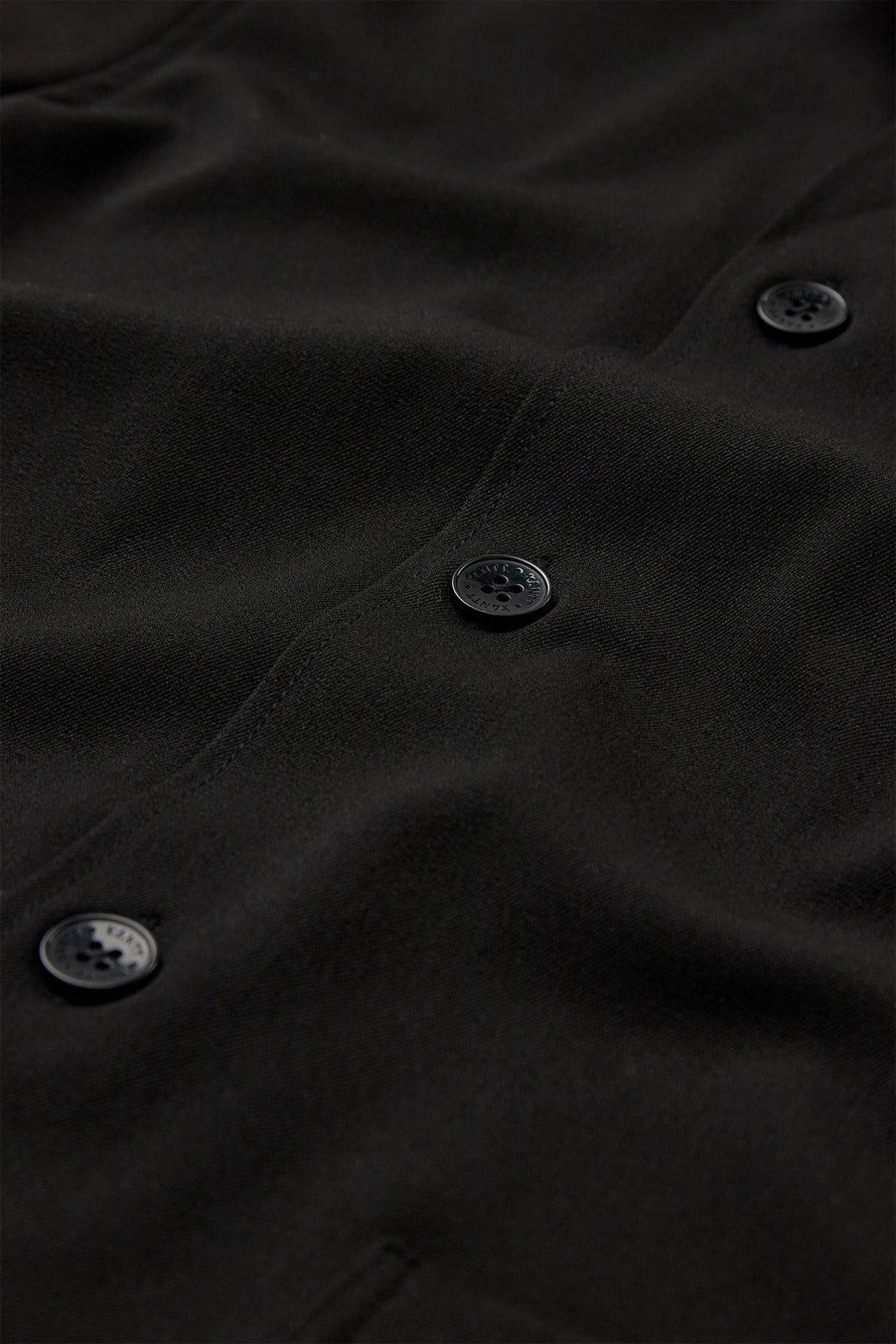 Sort strækbar overshirt med sorte knapper og synlige sømme på fronten.