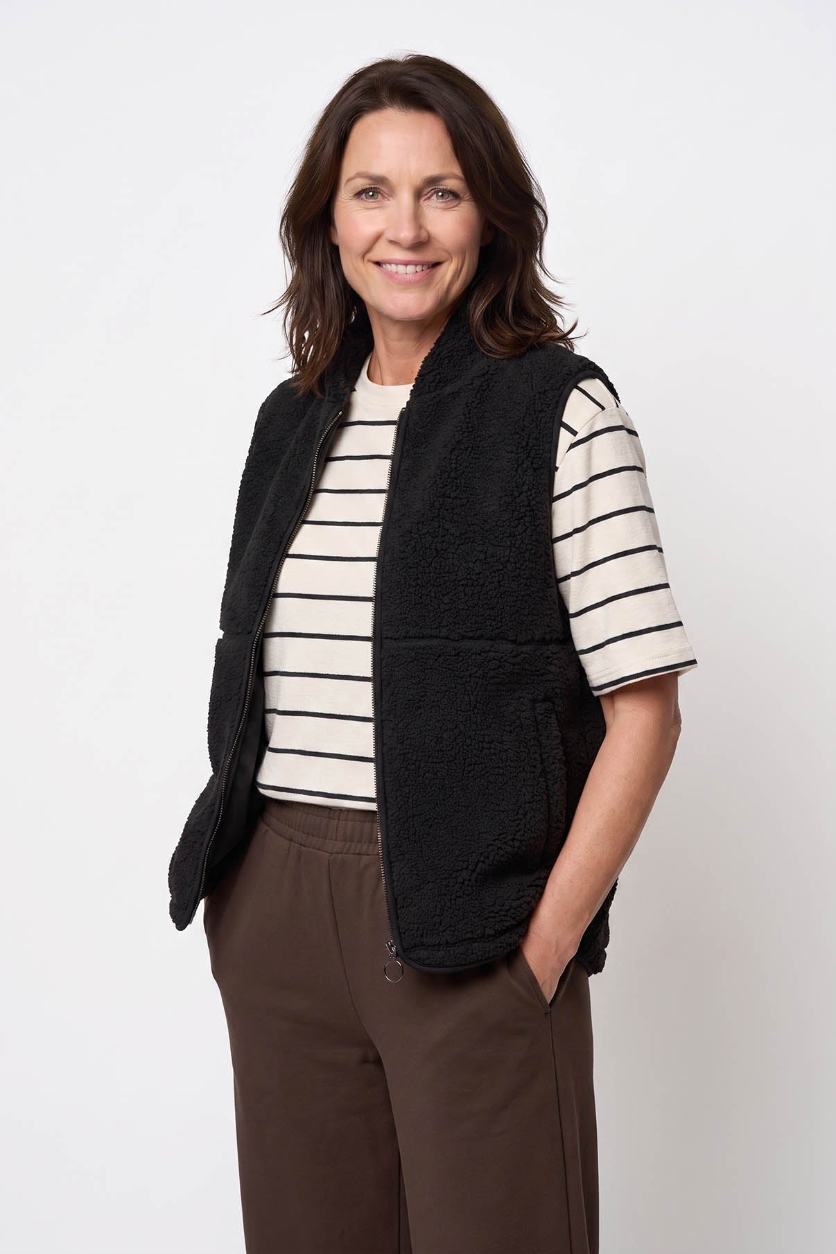 Sort teddy-vest med lommer, rund hals og slip-on design båret over stribet T-shirt.