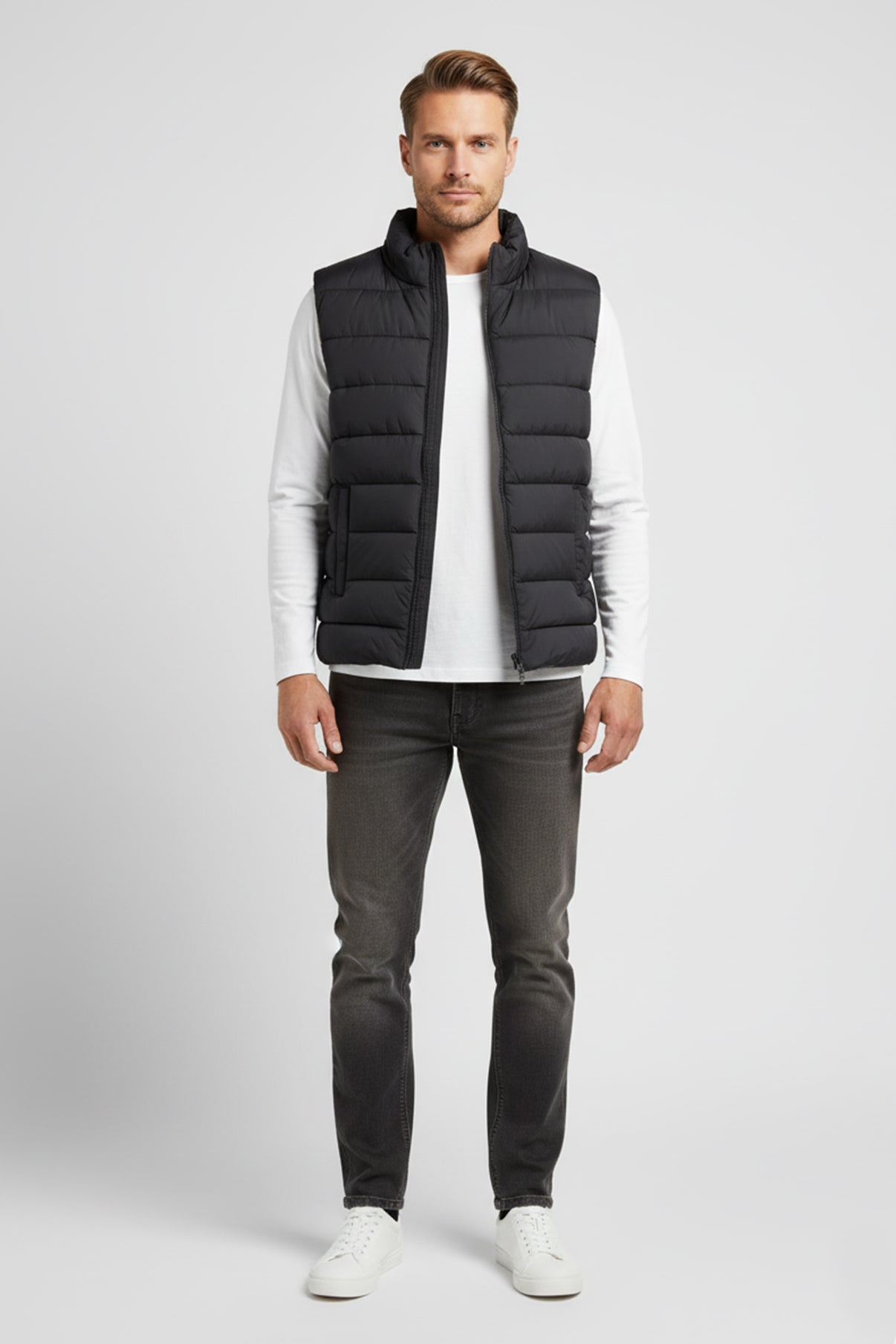 Let sort puffervest med stående krave og sidelommer, stylet med hvide sneakers og mørke jeans.