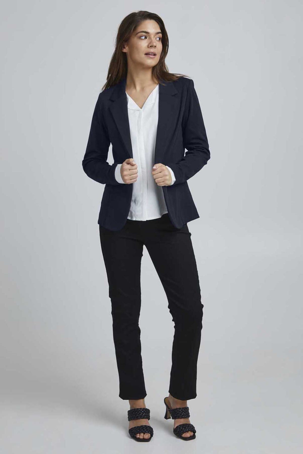 Sort klassisk blazer i regular fit med lange ærmer og jakkeslag, stylet med hvid bluse og sorte bukser.