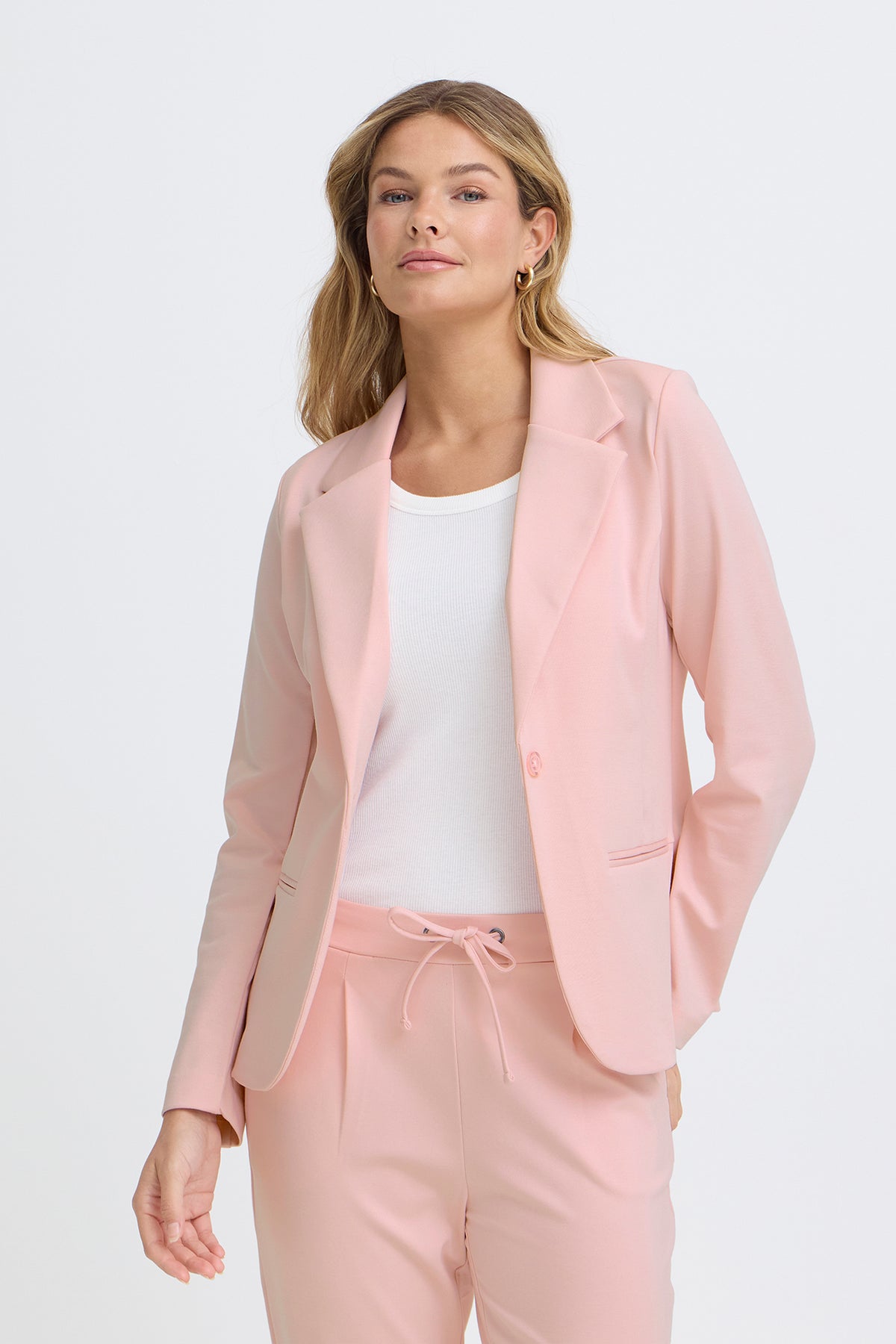 Lyserød klassisk blazer i regular fit med tre knapper og smalle revers, stylet med matchende bukser og hvid top.