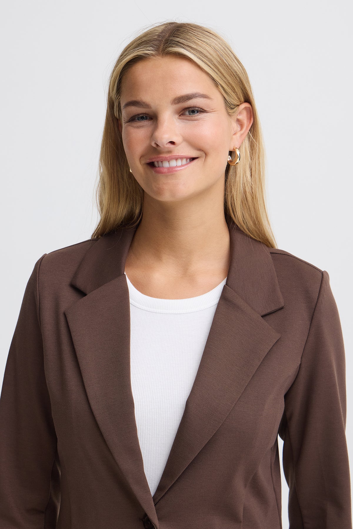 Brun klassisk blazer i regular fit med hakerevers og lange ærmer, båret over hvid top.