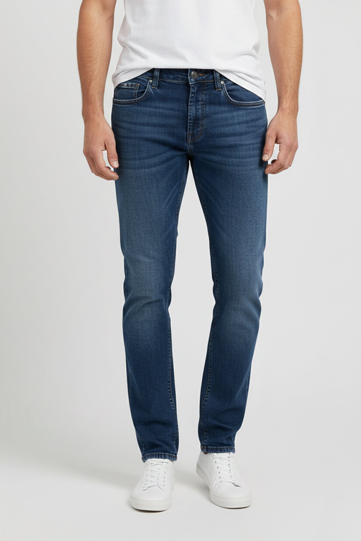 Mørkeblå stretch jeans med smal pasform og klassiske lommer, brugt med hvid T-shirt og hvide sneakers.