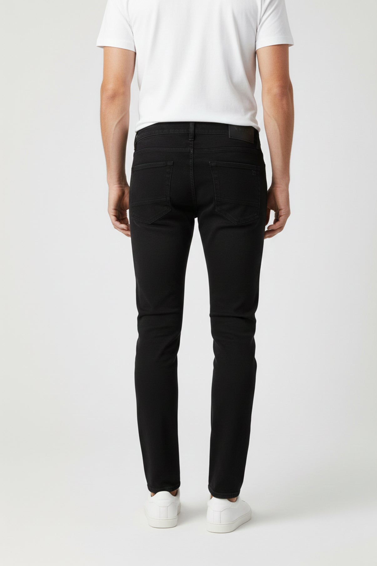 Ultra sorte stretch jeans med tætsiddende pasform og baglommer, båret med hvid t-shirt og hvide sneakers.