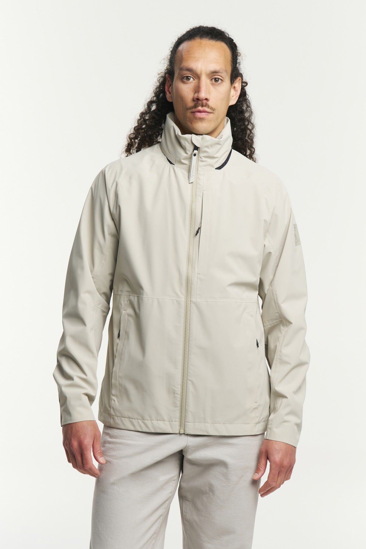 Beige funktionel skaljakke med høj hals og lynlås foran, glat stof og sidelommer.