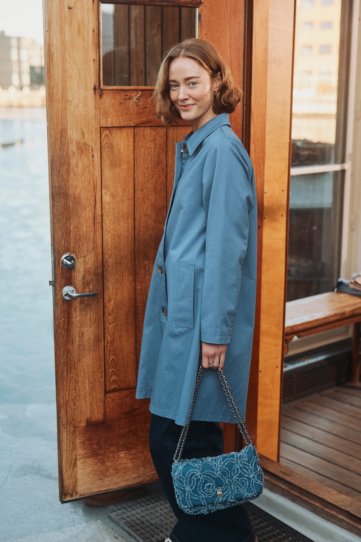 Blå trenchcoat med lange ærmer og skjulte knapper, kombineret med blå taske i quiltet stof.