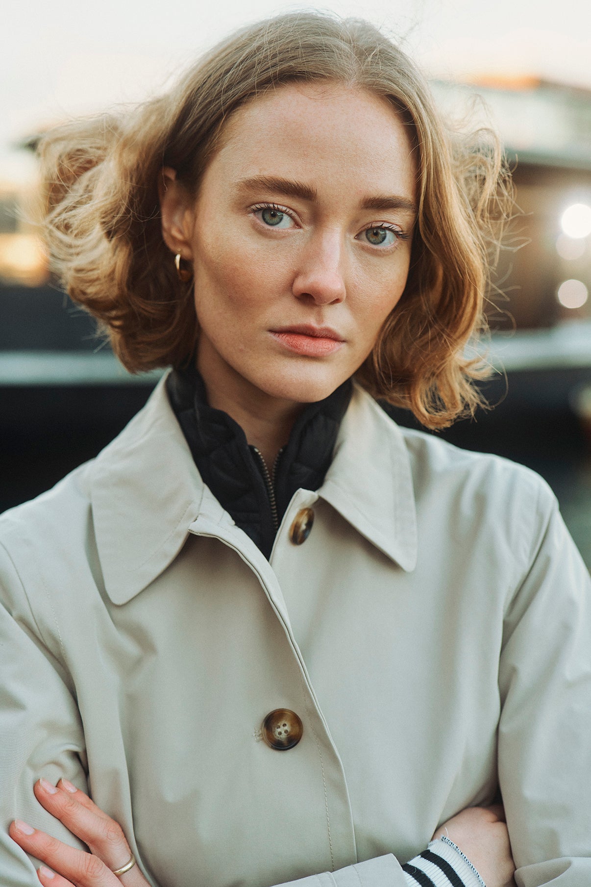 Kvinde iført sort let quiltet vest med lynlås og høj krave under beige trenchcoat med knapper.