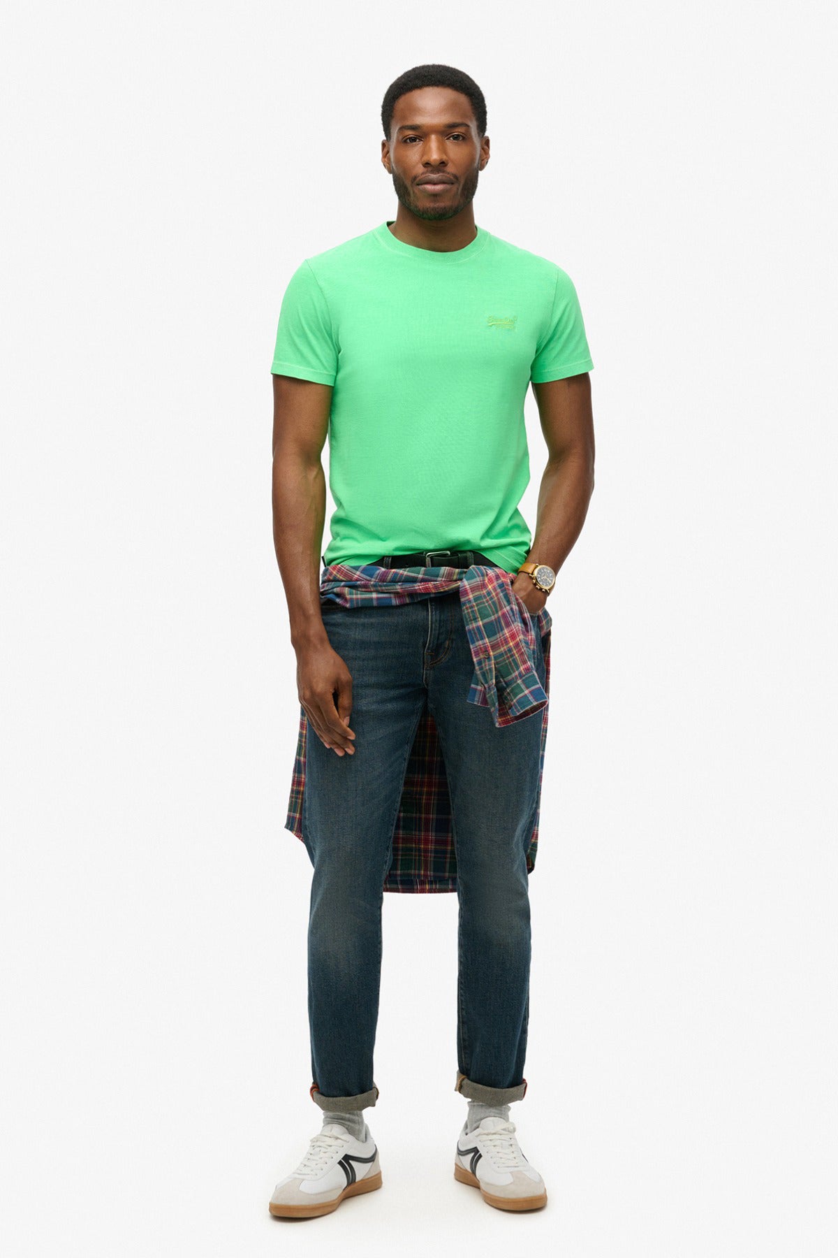 Neon limegrøn t-shirt med ESSENTIAL-logo, kortærmet, slank pasform, mørkeblå jeans, ternet skjorte bundet om livet.