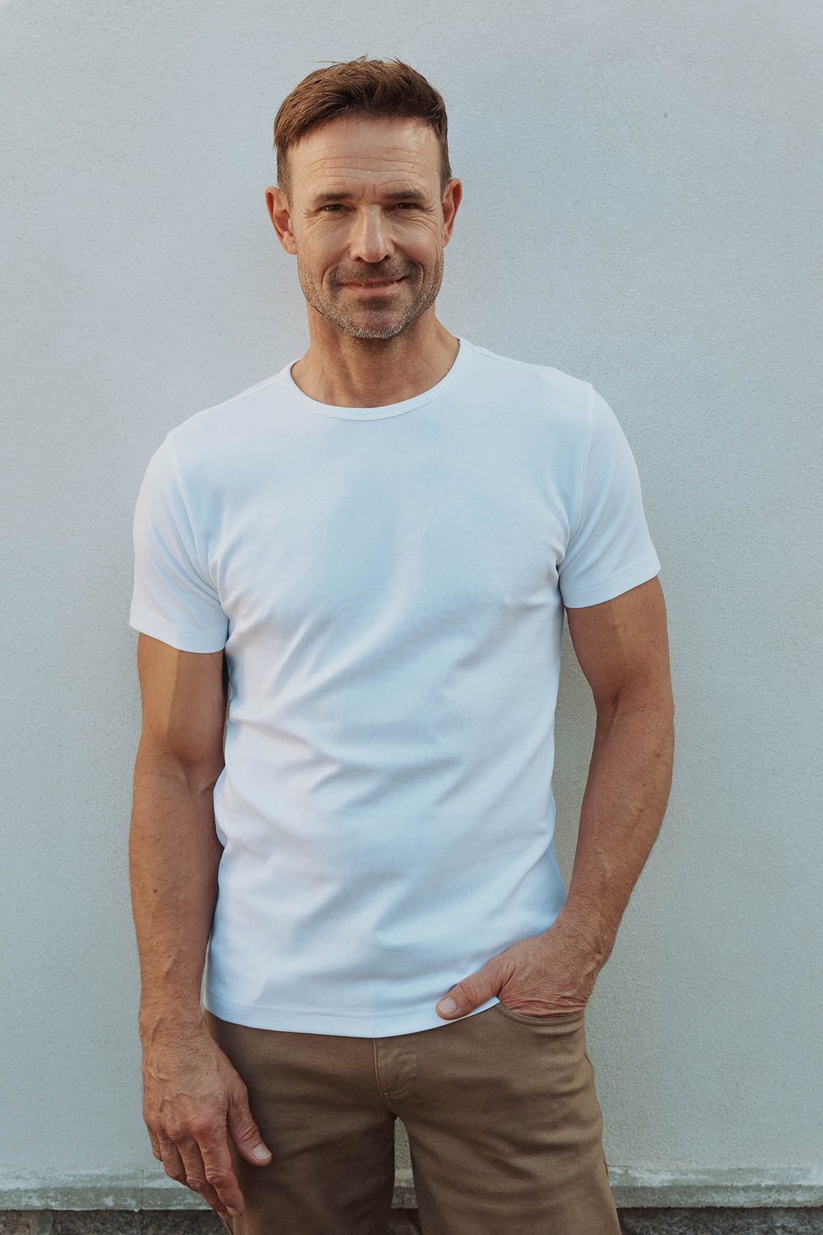 Mand i enkel hvid basic T-shirt med korte ærmer og rund hals samt brune bukser.