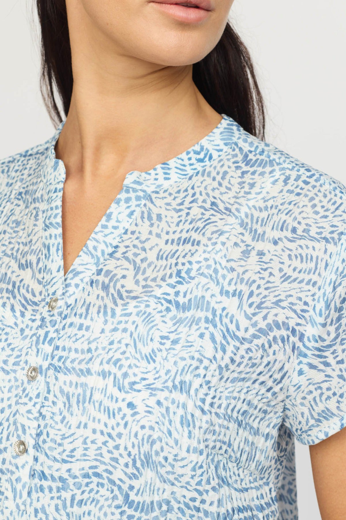 Kortærmet bluse med lys blå og hvid abstrakt prikket print og V-udskæring.