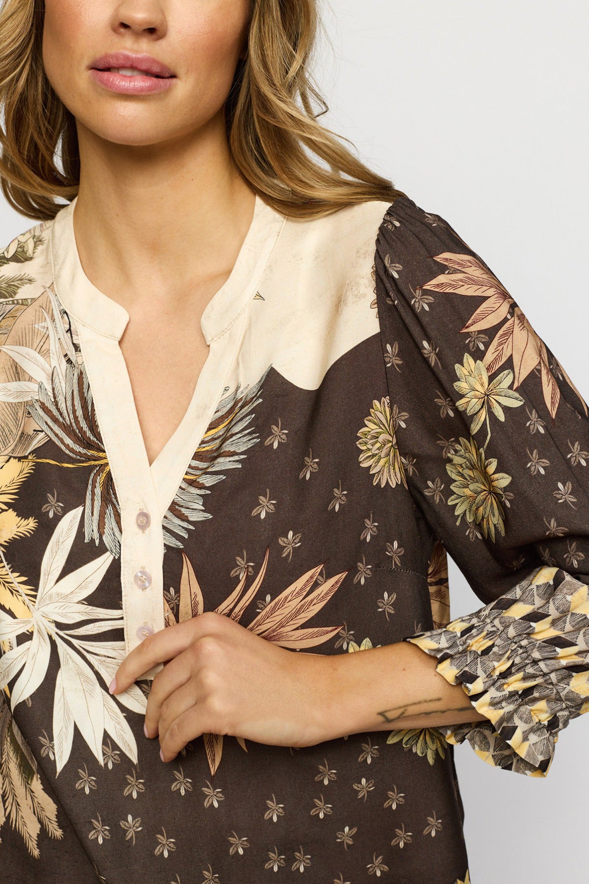 Mønstret bluse i sandfarvet med brune og beige blomster, trekvartærmer med rynkede manchetter og knapdetalje ved halsen.