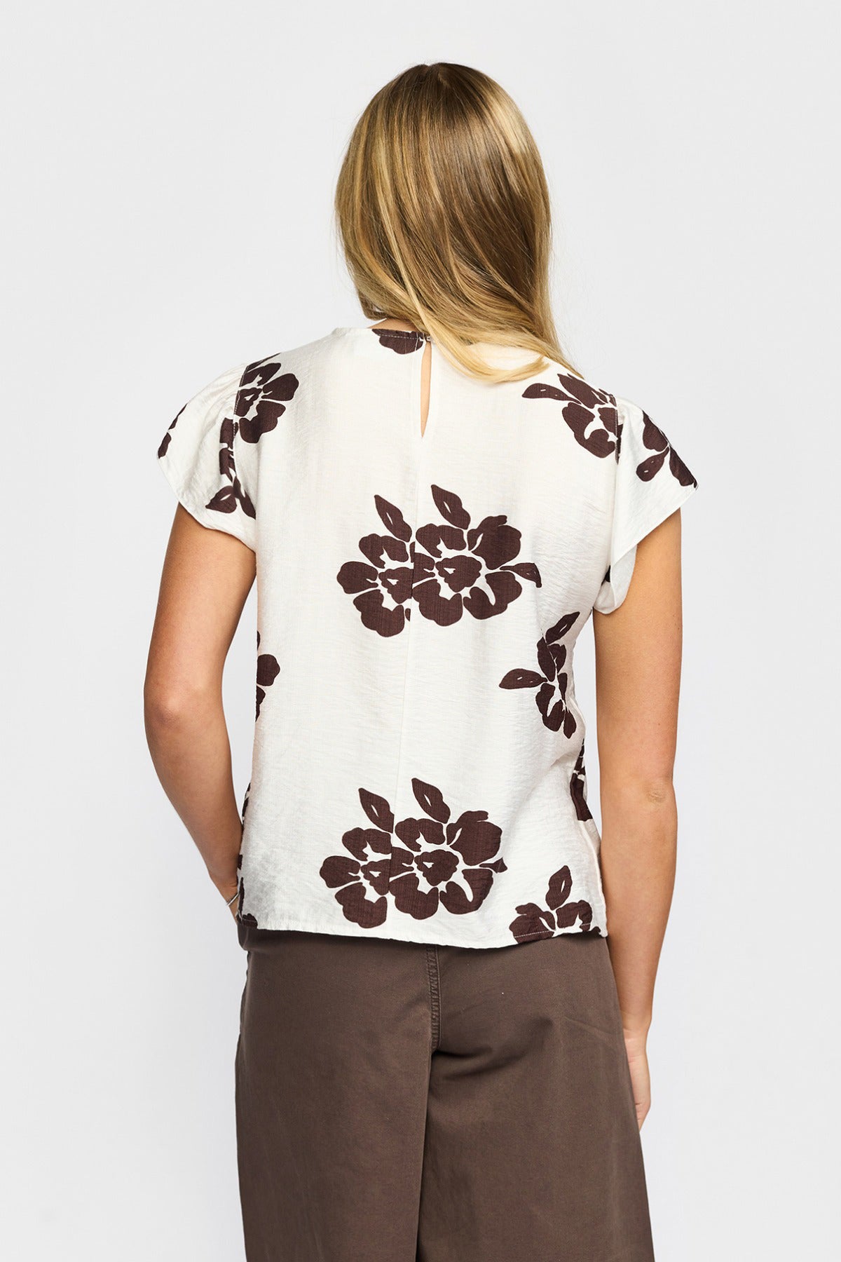 Hvid kortærmet bluse med brune blomsterprint og let rundet hals bagfra.