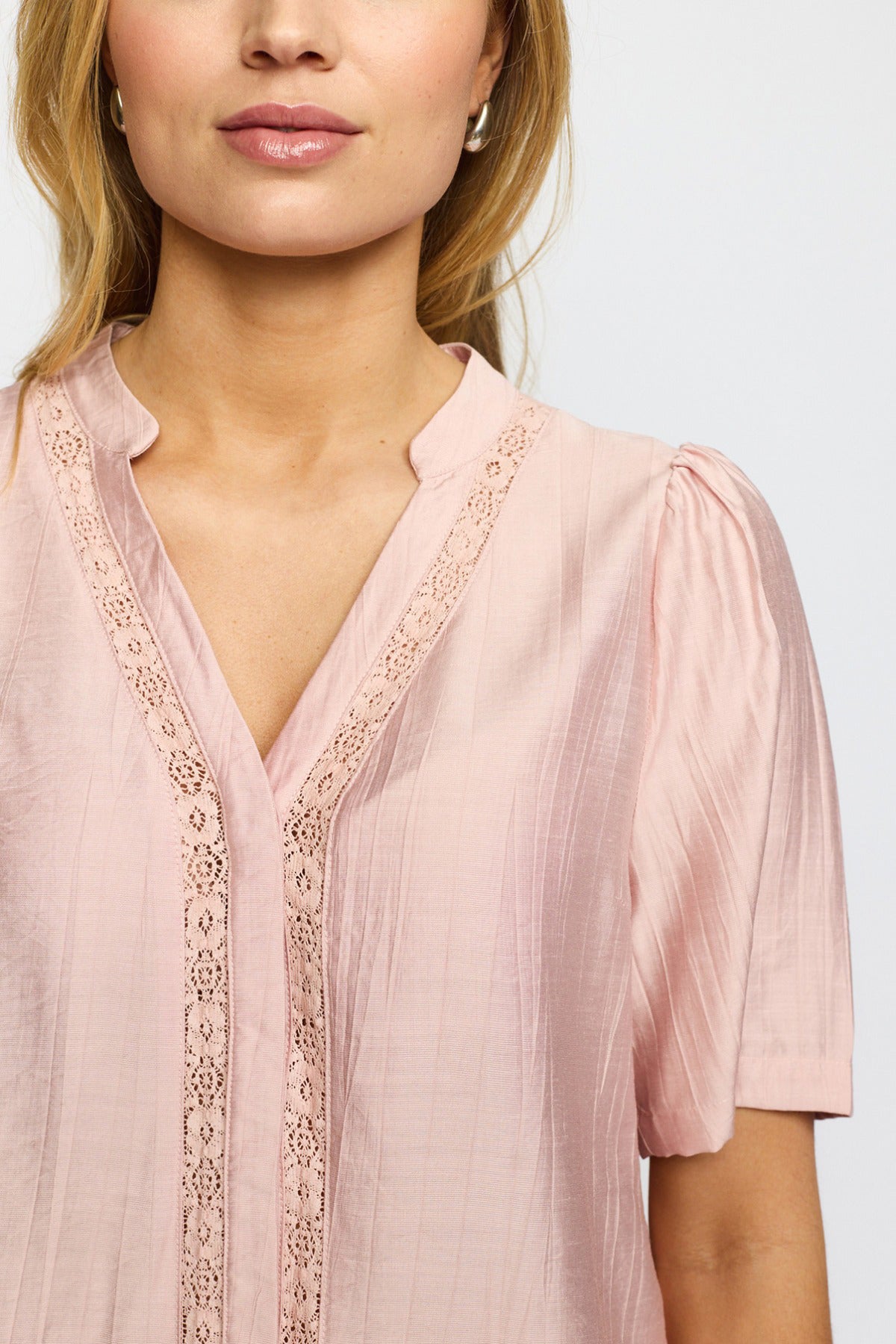 Lys rosa kortærmet bluse med v-hals og blondekant langs udskæring og frontpanel.