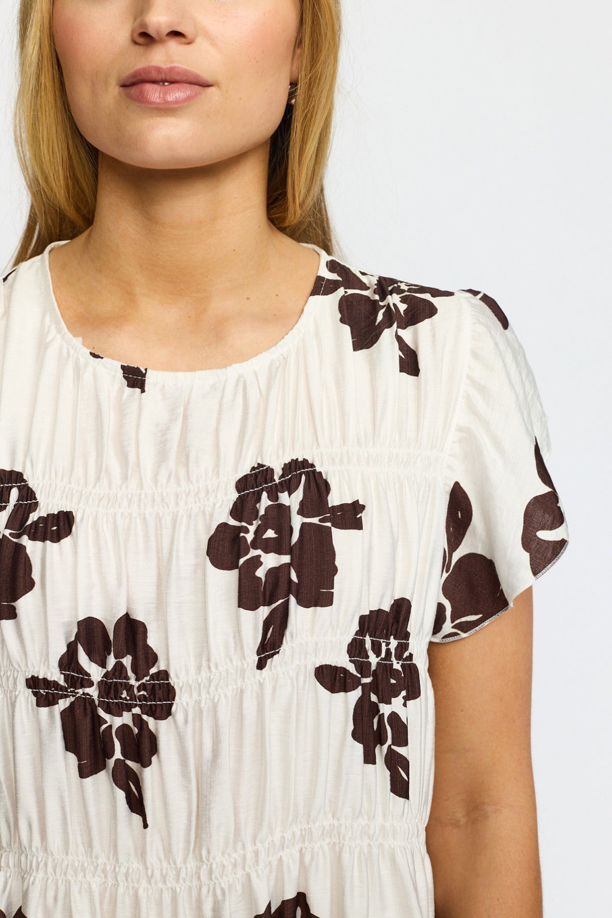 Kortærmet hvid kjole med brunt blomsterprint og let rynkede detaljer.