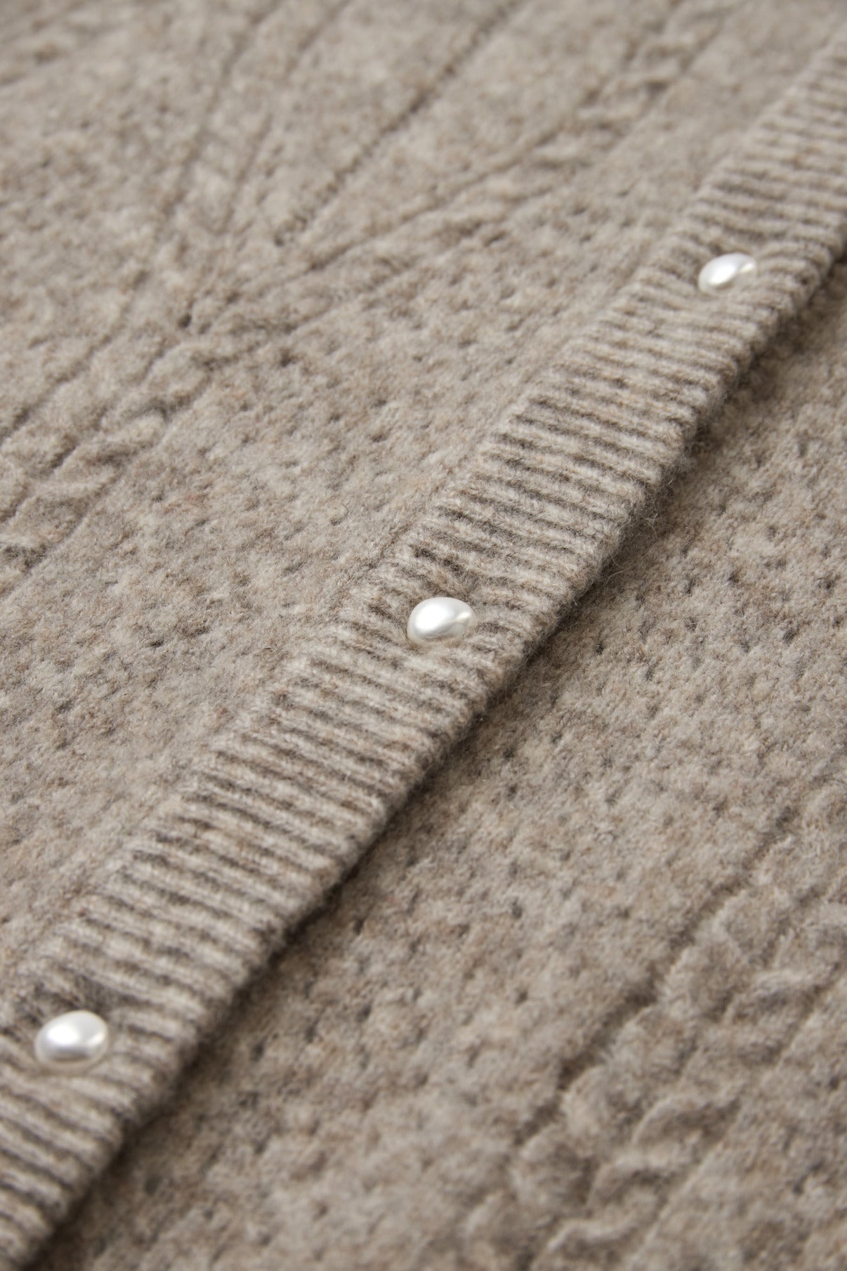 Beige strikcardigan med flettemønster og perleknapper i forløbende række.
