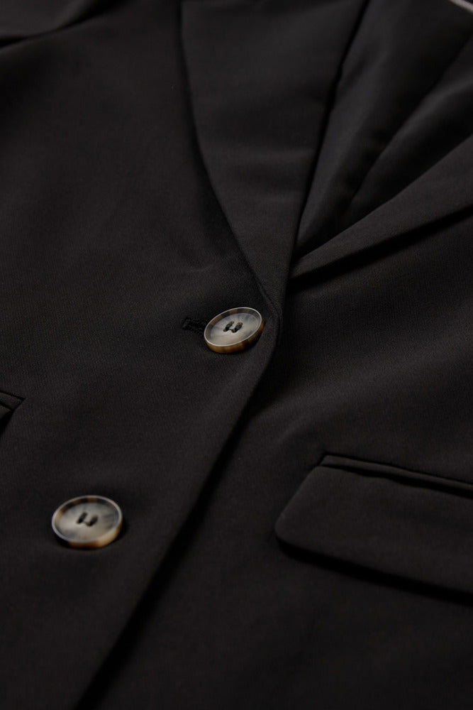 Sort klassisk blazer med revers, to knapper og sidelommer.