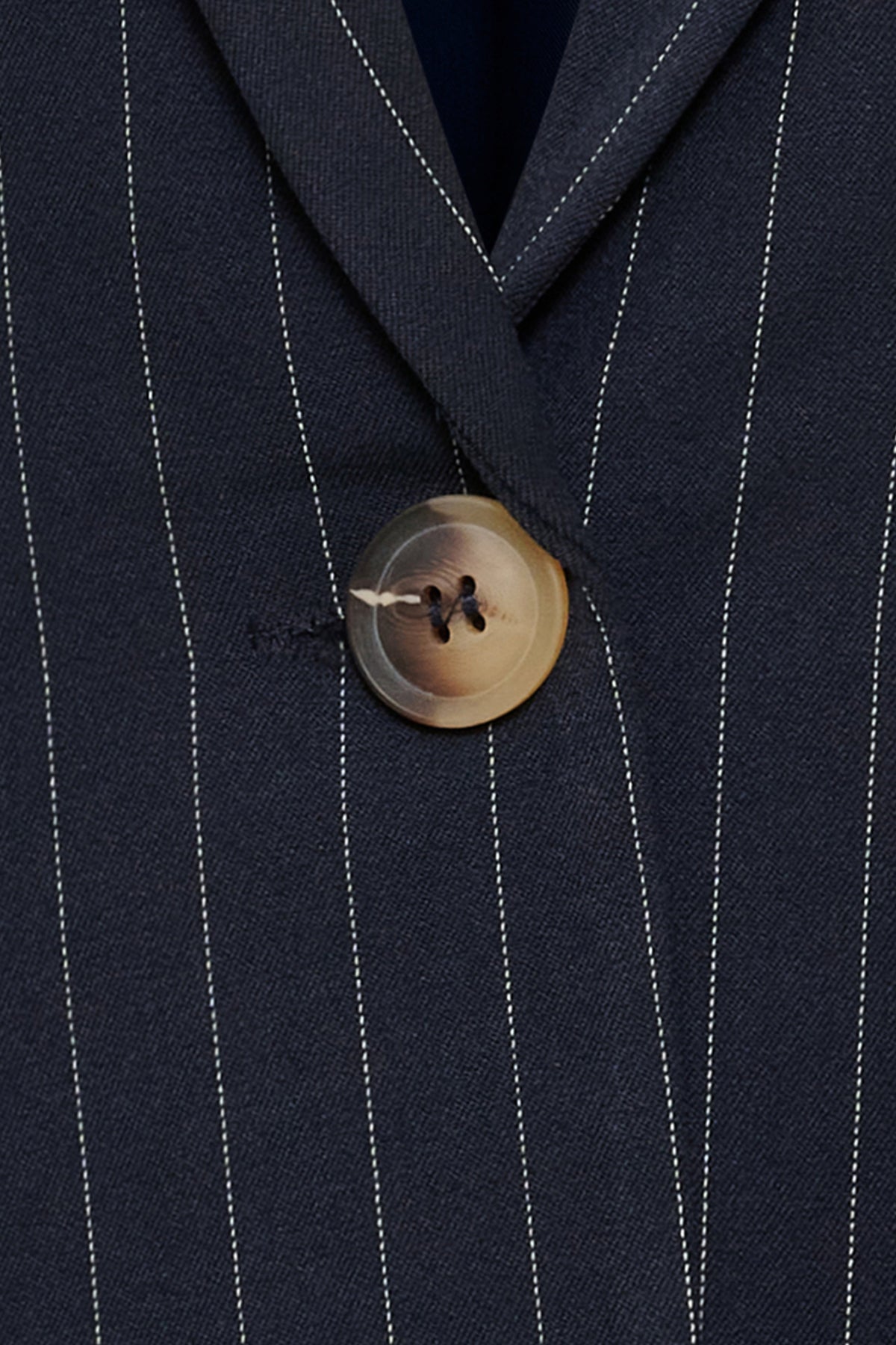 Navyblå blazer i klassisk snit med tynde hvide nålestriber og stort brunligt knapdetalje.