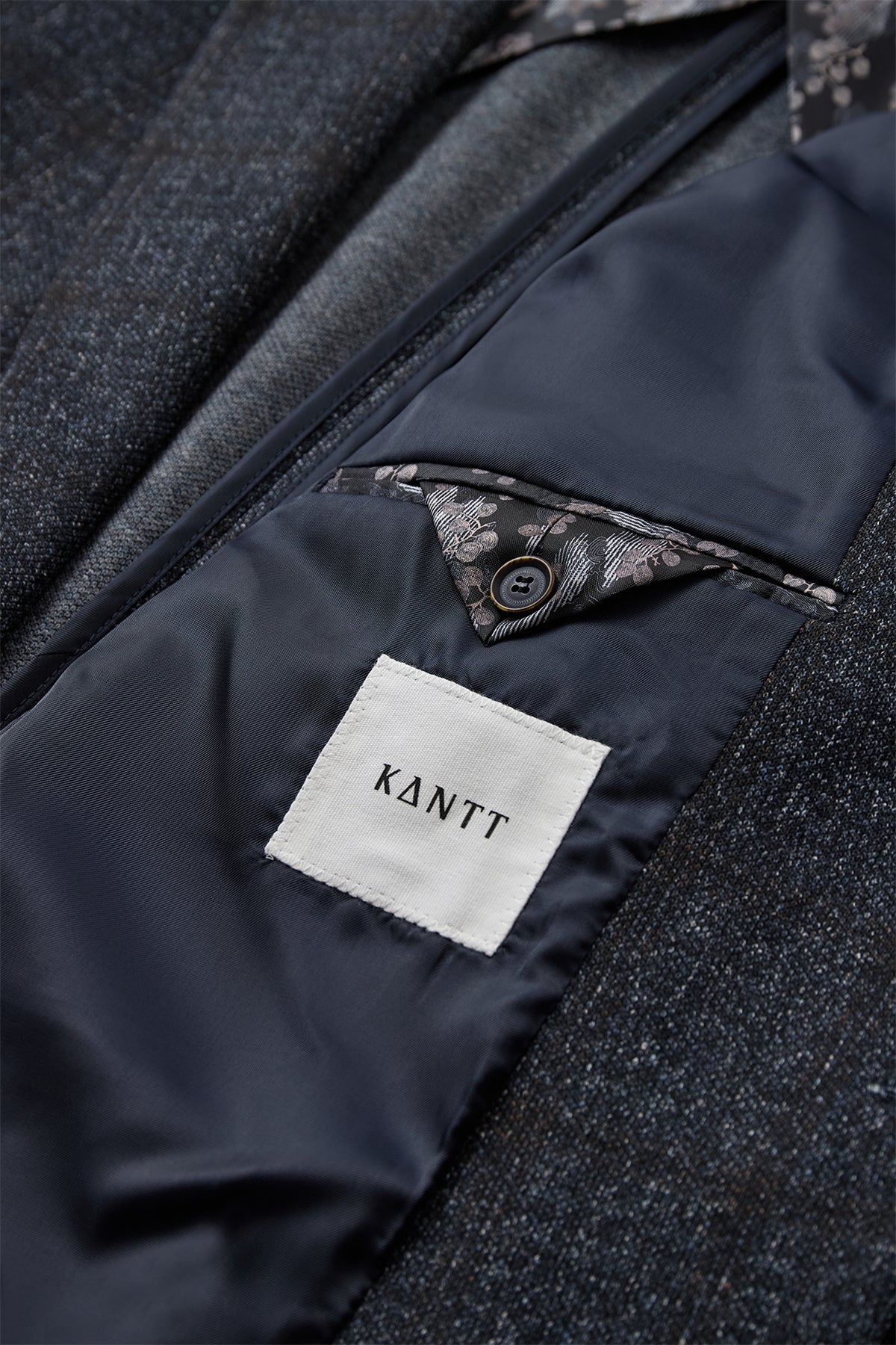 Mørkegrå blazer med fin struktur og glat navy foring med inderlomme og knapdetalje.