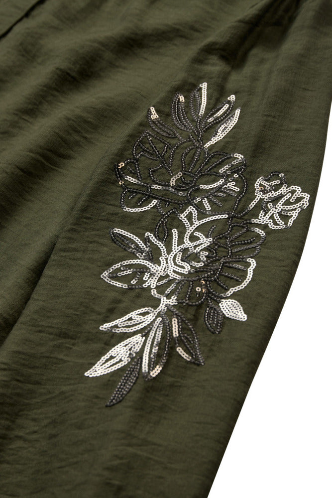 Mørkegrøn bluse med glinsende blomsterpailletter i sorte og hvide nuancer, blødt stof.