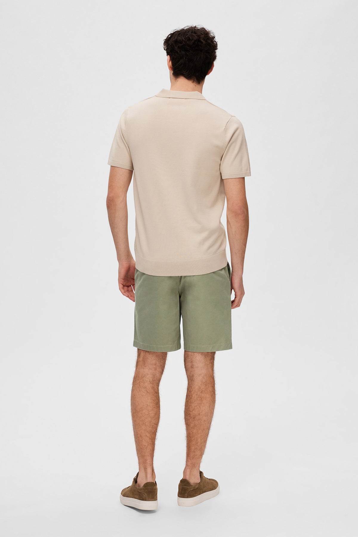 Mand med beige strikket polo med korte ærmer og grønne shorts set bagfra.