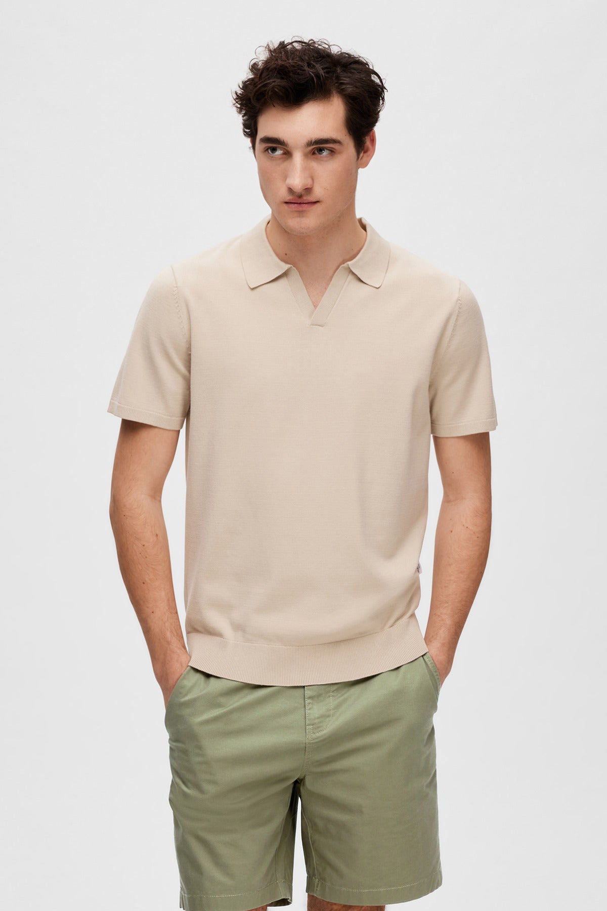 Beige kortærmet strikket polo med krave og løs pasform på mand, styling med grønne shorts.