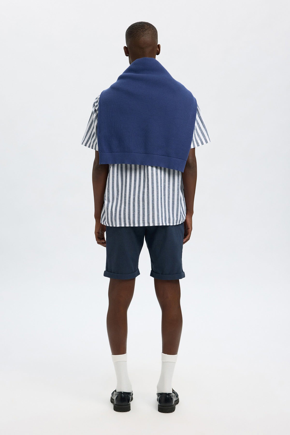 Mørkeblå strækbare shorts med lommer på model set bagfra, kombineret med sort-hvid stribet skjorte og blå trøje over.