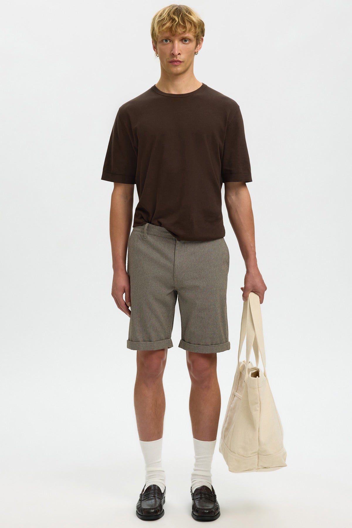 Strækbare shorts i beige med lommer, kombineret med brun T-shirt, hvide sokker og sorte sko, bærer netpose i naturfarve.