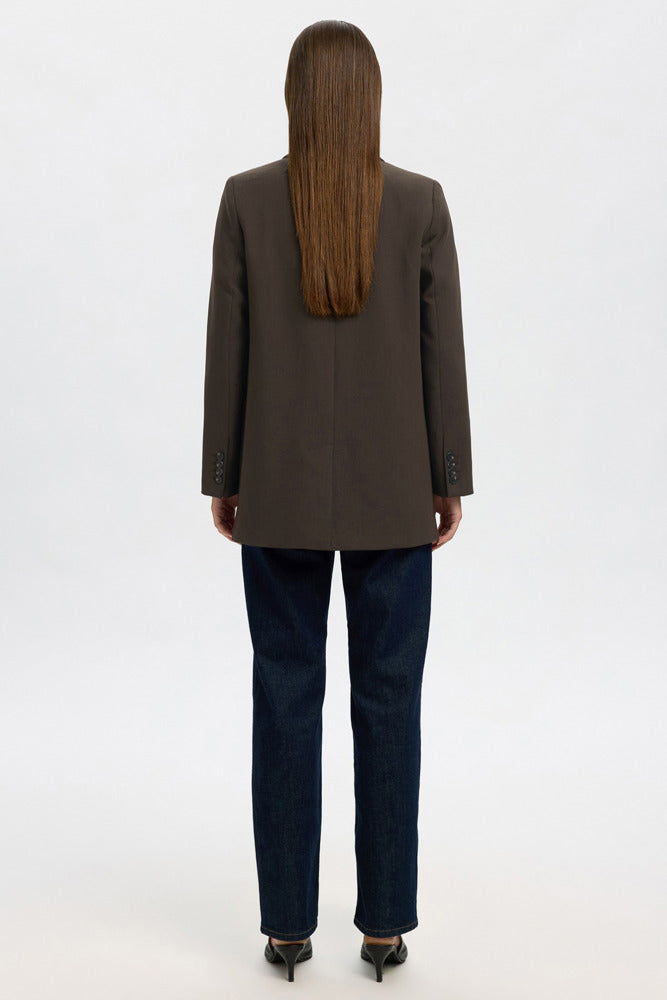 Brun afslappet blazer med revers set bagfra, kombineret med mørkeblå bukser og sorte sko.
