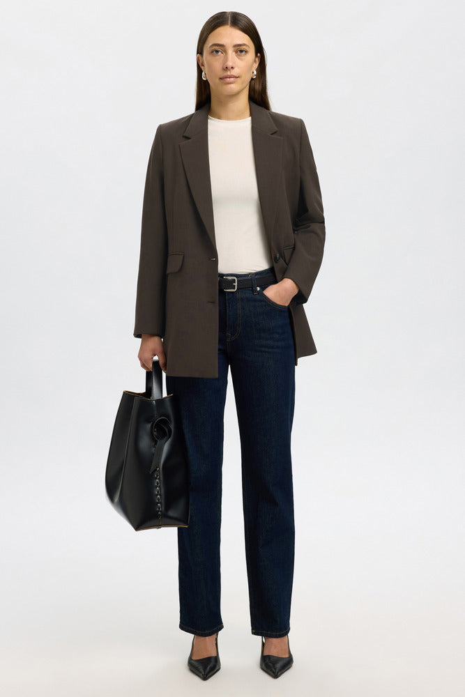 Mørkebrun afslappet blazer med revers, lang pasform og lomme detaljer, stylet med mørkeblå jeans og hvid top.