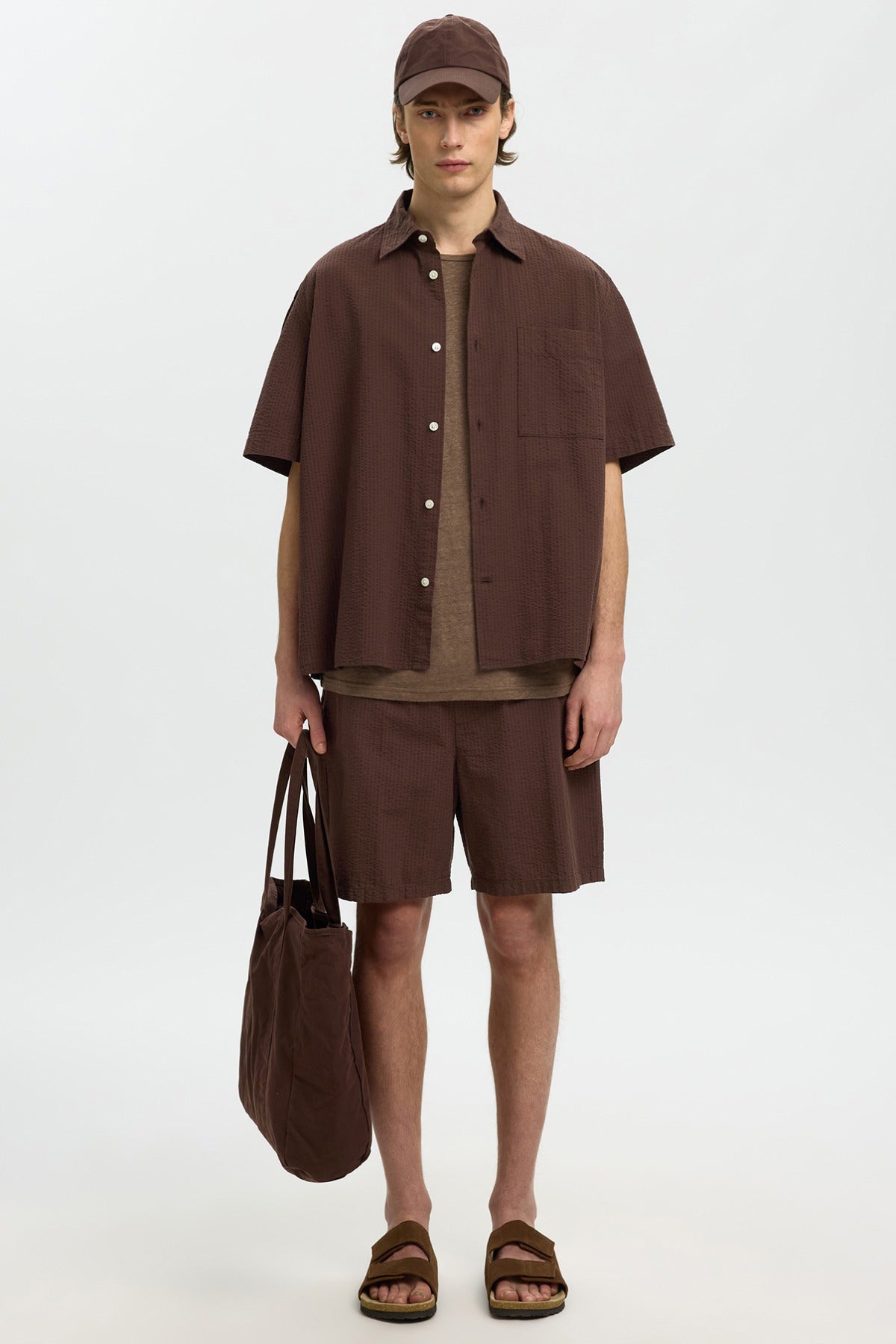 Mørkebrun kortærmet skjorte med knapper, matchende shorts, brunt net-taske og sandaler.