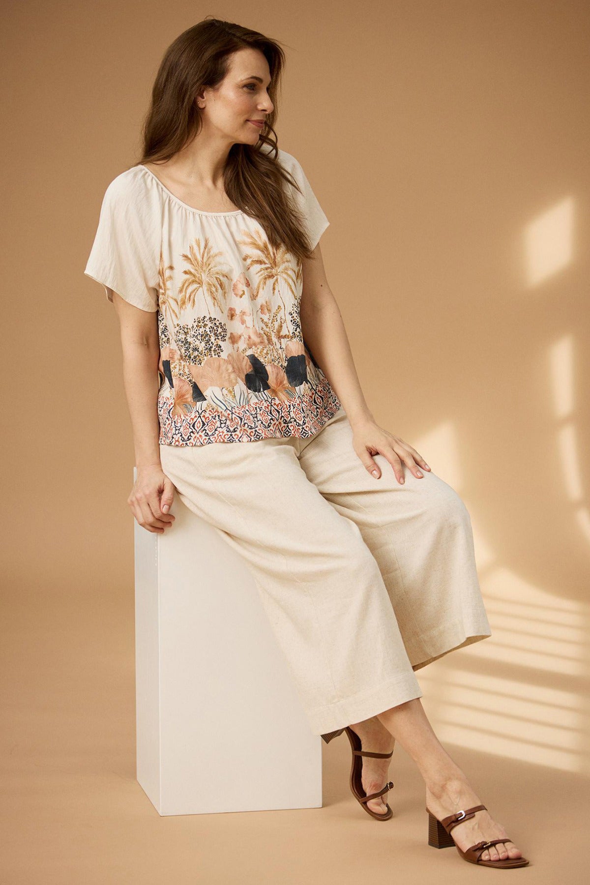 Kortærmet multifarvet bluse med rynket kravedetalje og blomsterprint på beige baggrund.