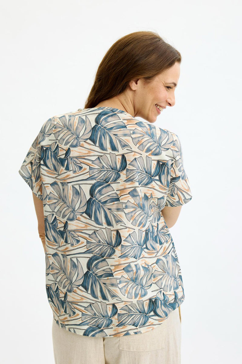 Bluse med kort ærme i beige med blå og grønne bladprint og guldbuton detalje bagpå.