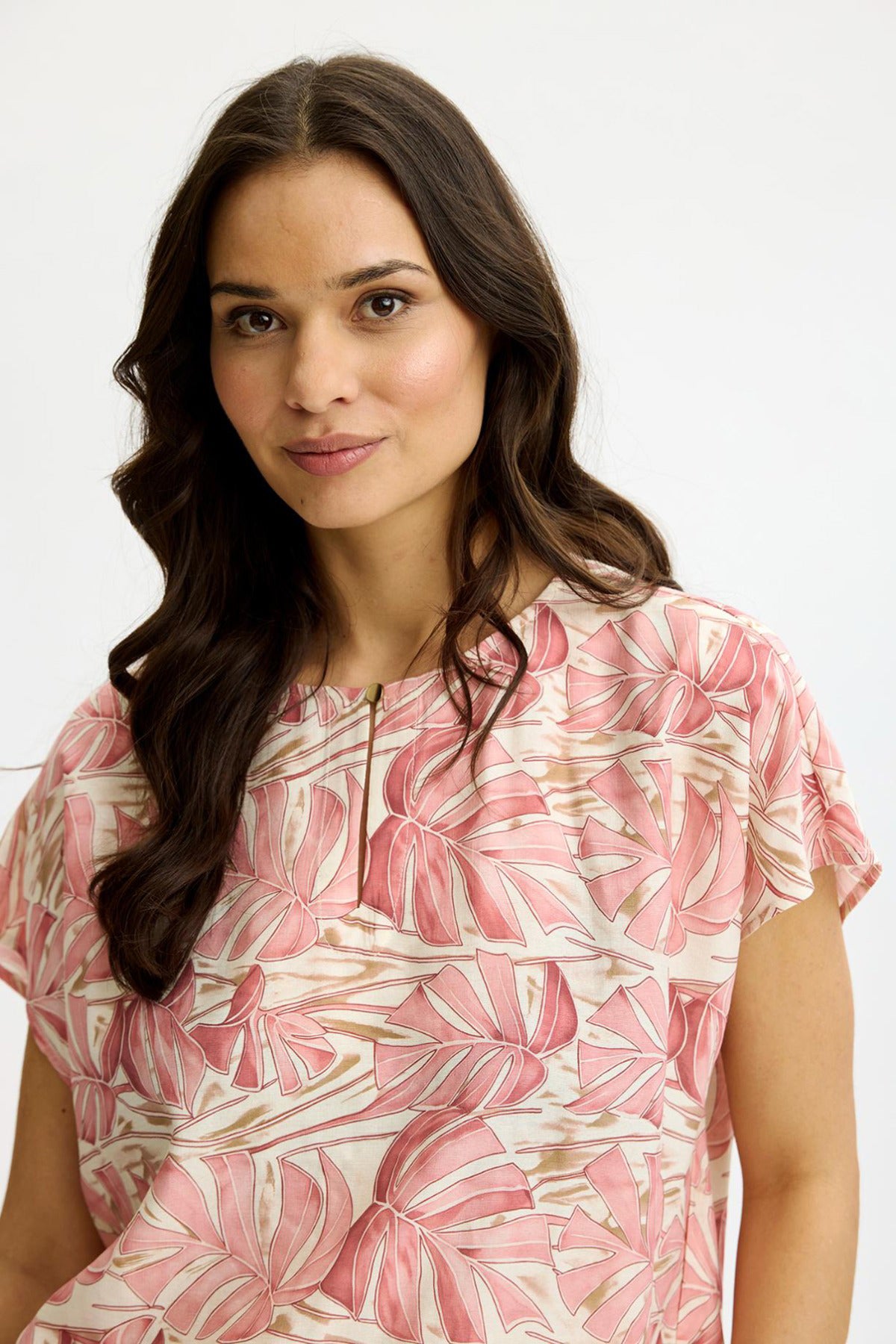 Rosa bluse med lyse guldknapper og bladprint i bløde nuancer.