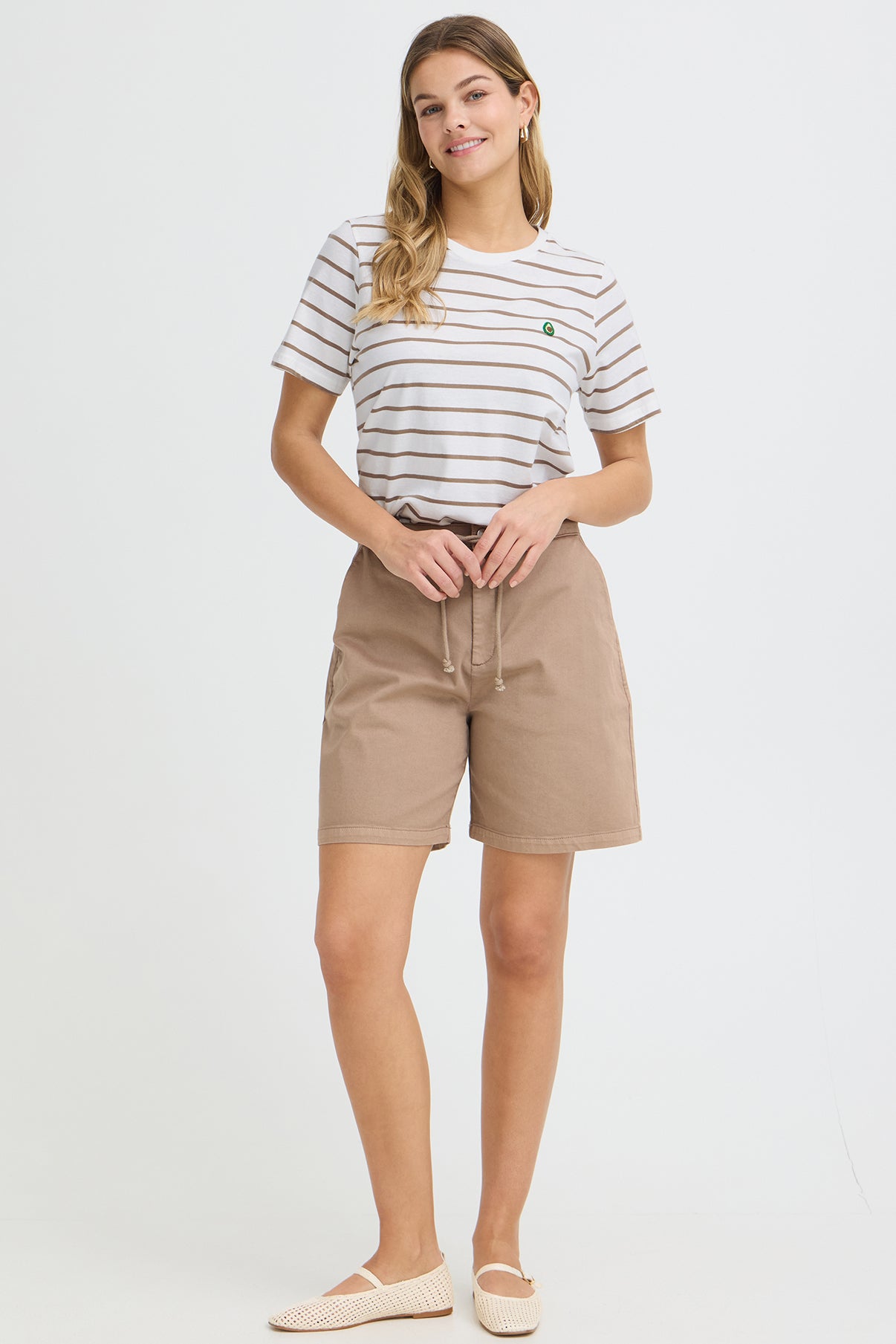 Hvid t-shirt med tynde sorte og rosa striber og broderet detalje, stylet med beige shorts.