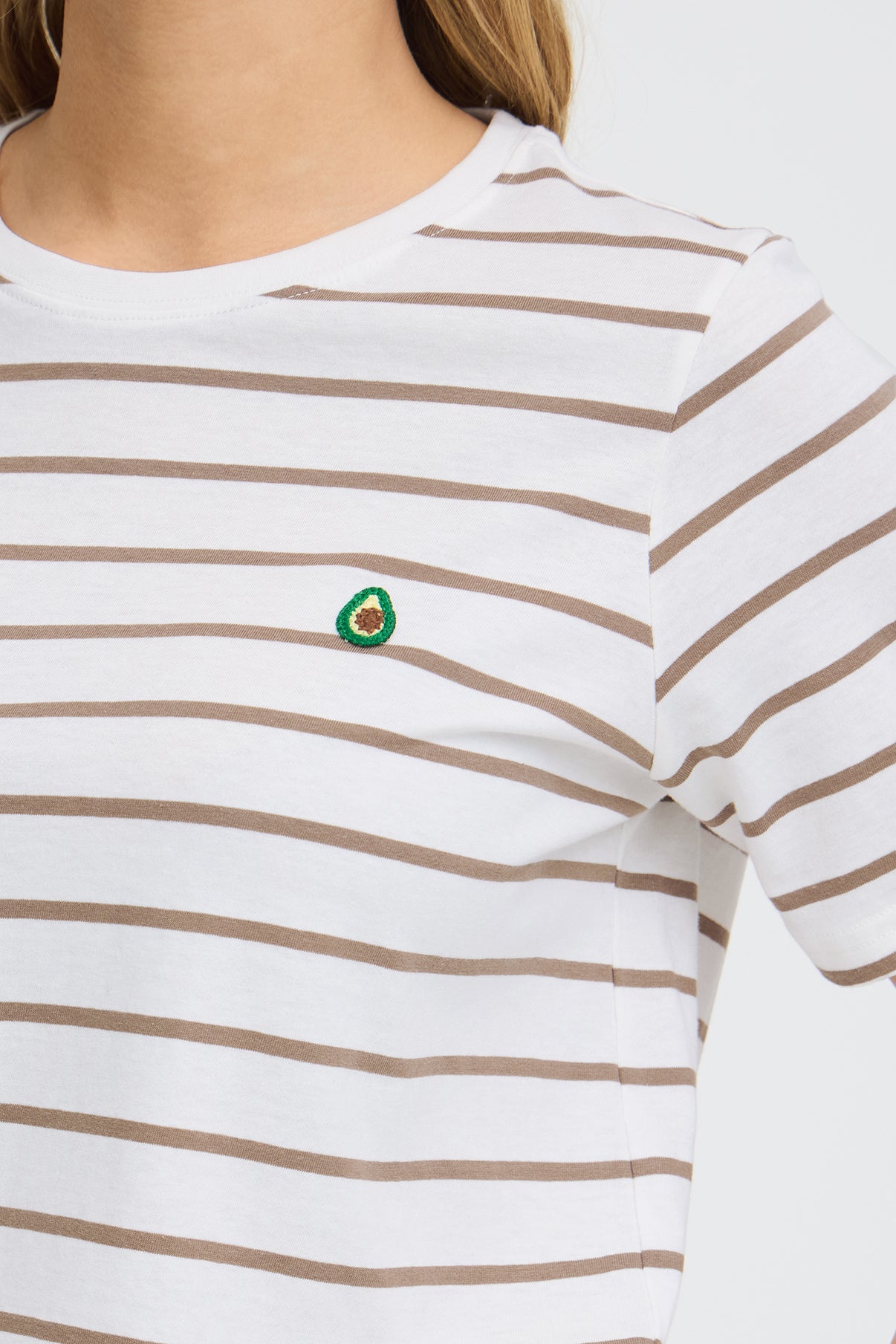 Hvid t-shirt med smalle brune striber og lille avocado broderi ved brystet.