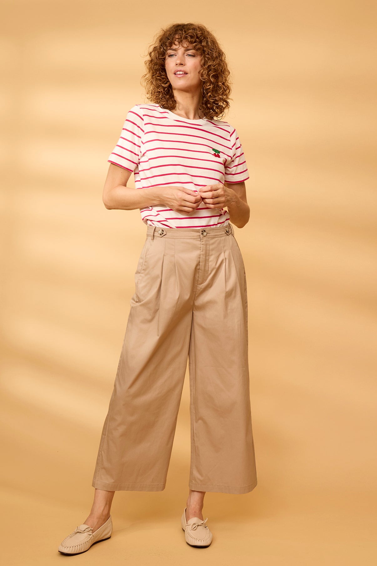 Hvid t-shirt med rosa striber og broderet detalje, khaki brede bukser og cremefarvede slip-on sko.