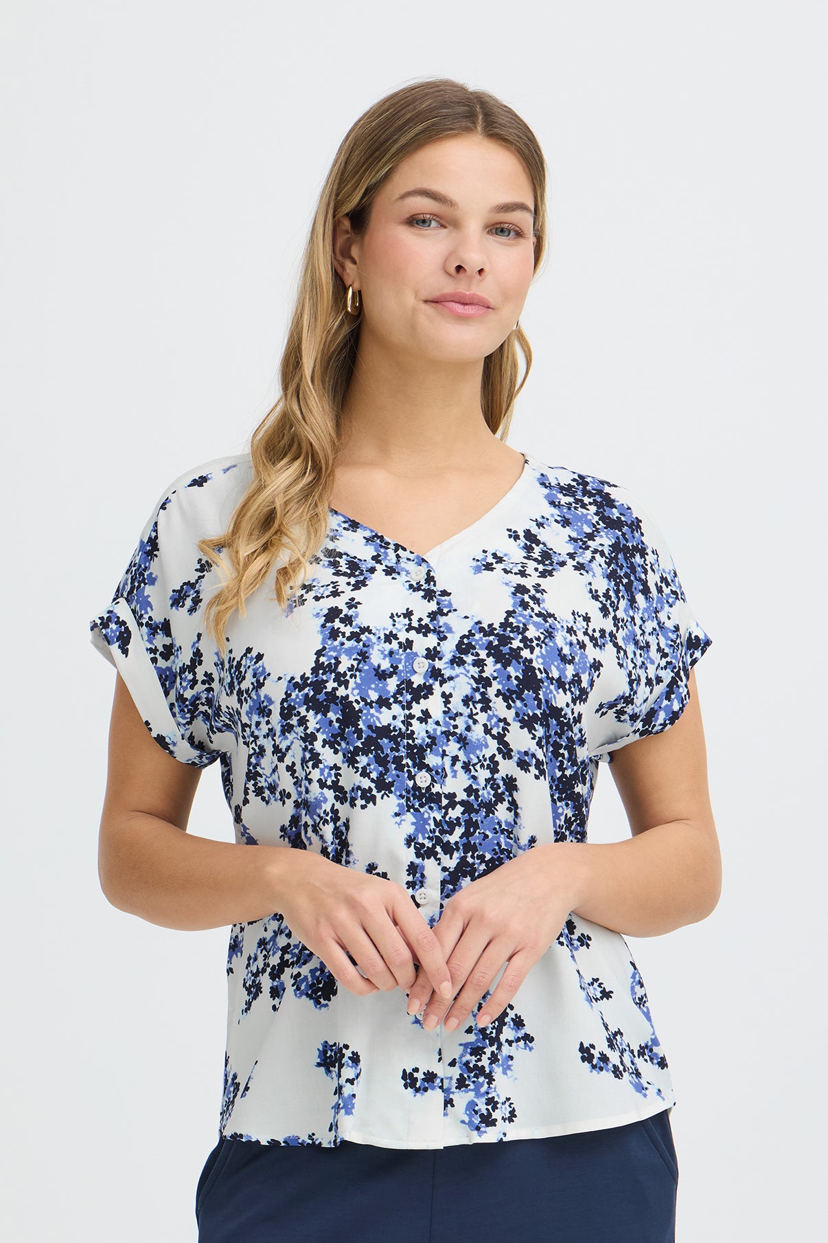 Kortærmet hvid skjortebluse med blå blomstermønster og V-hals.