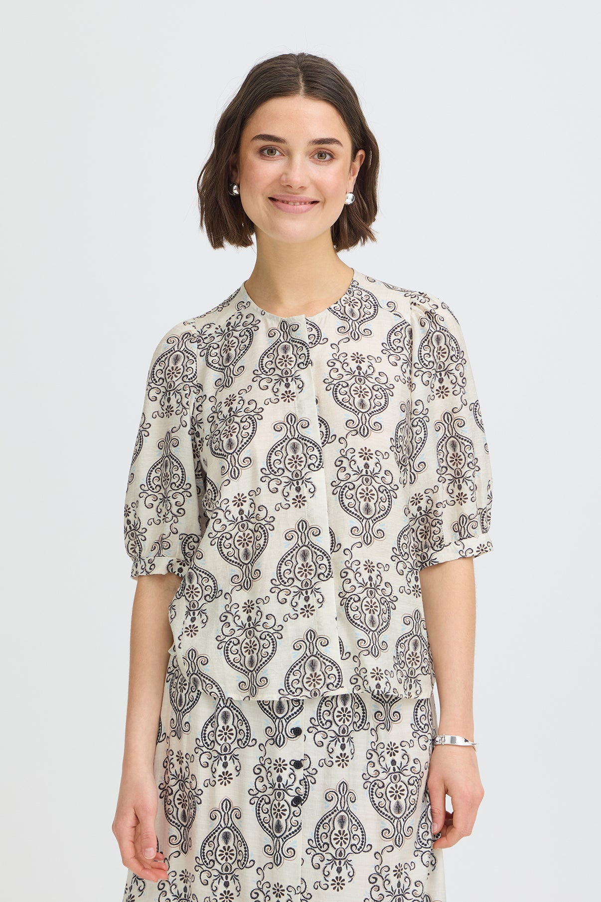 Kortærmet skjortebluse med hvid bund og sort boho blomstermønster, rund hals og let puffede ærmer.