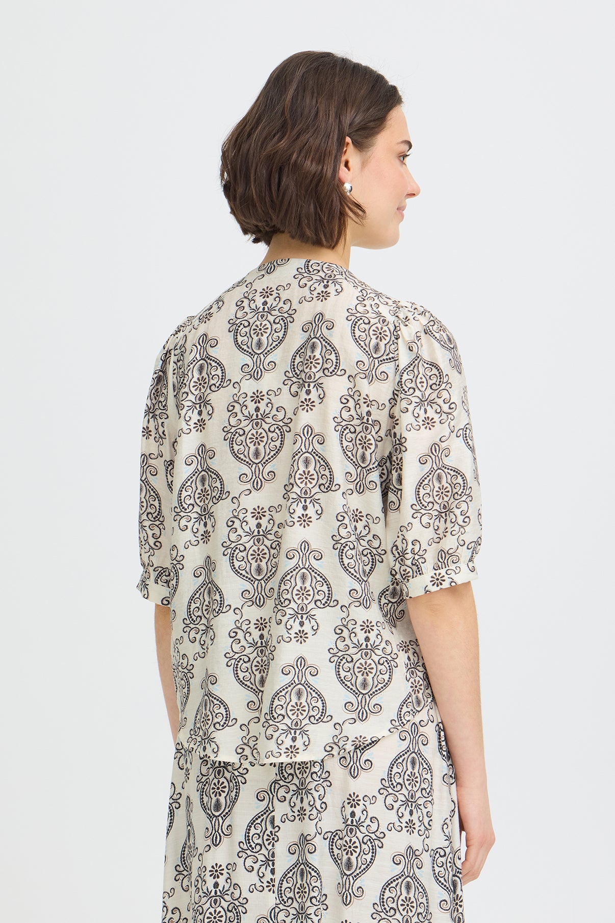 Kortærmet skjortebluse med hvid bund og sort boho-motiv, løs pasform bagfra.