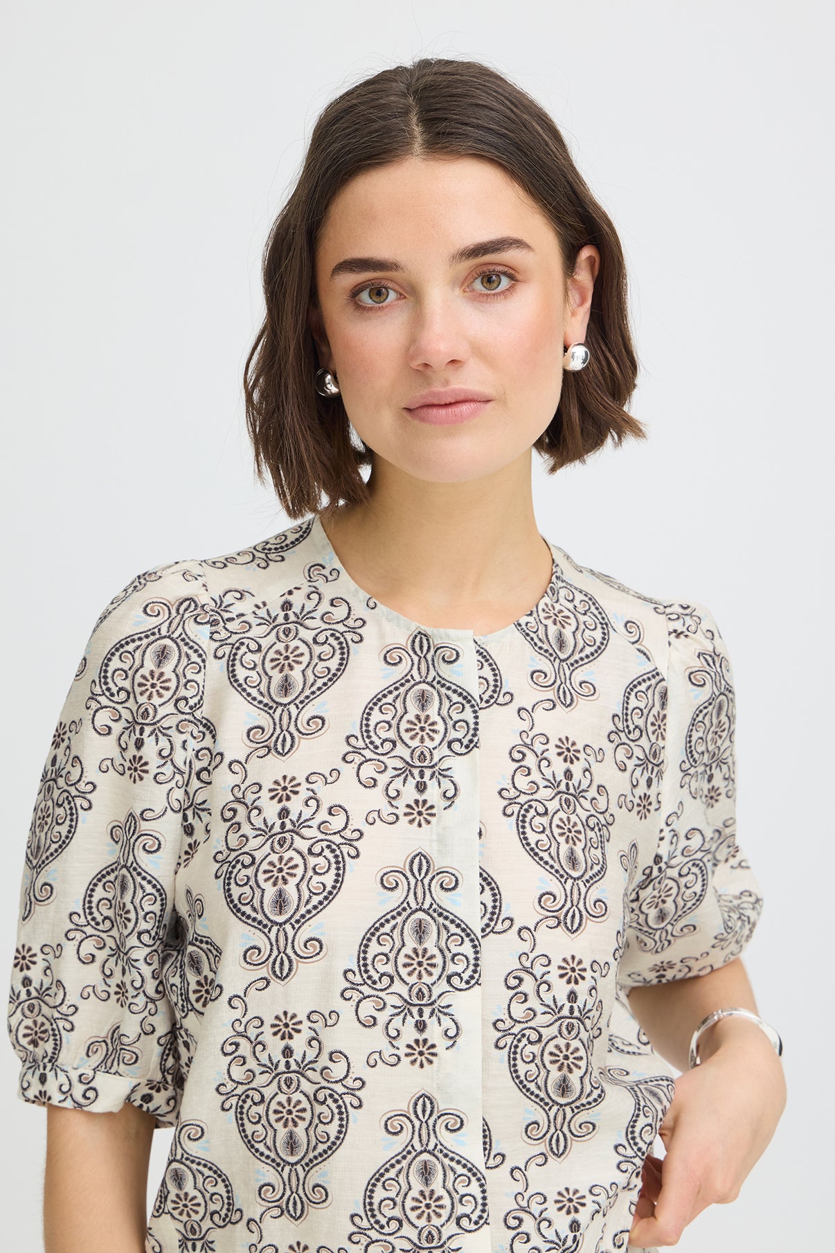 Kortærmet skjortebluse i hvid med sort boho-inspireret mønster og rund hals.