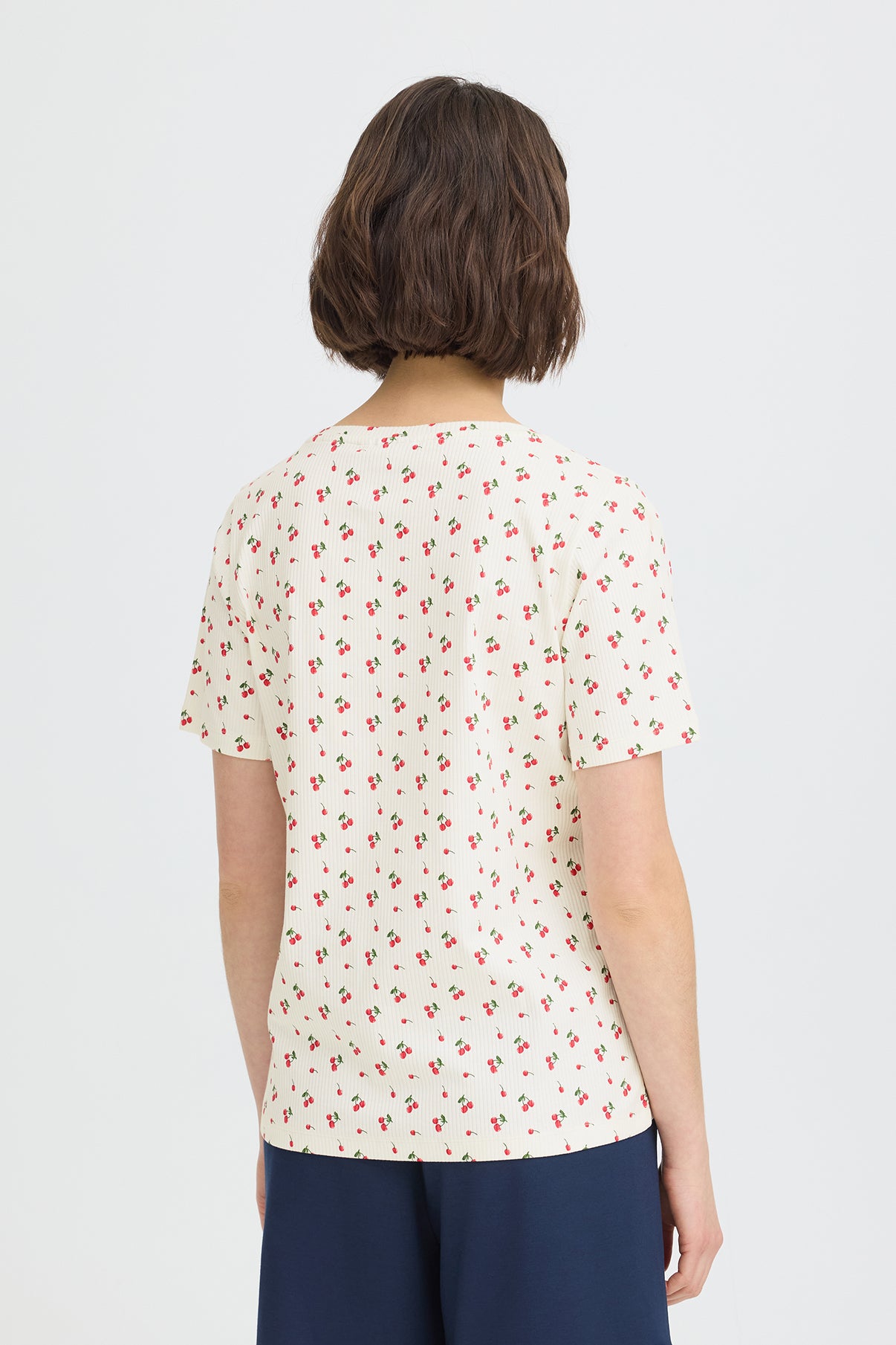 Kortærmet hvid t-shirt med små røde kirsebærprint, set bagfra.