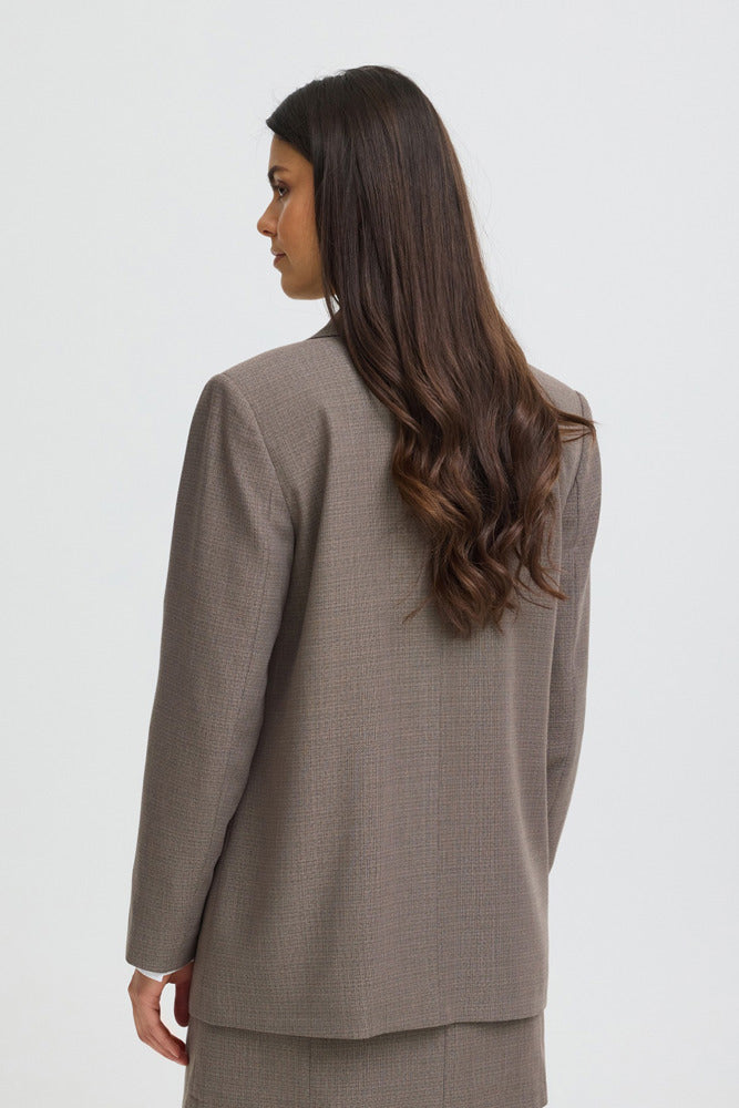 Kvinde iført driftwood melange dobbeltradet blazer set bagfra med langt, mørkt hår.